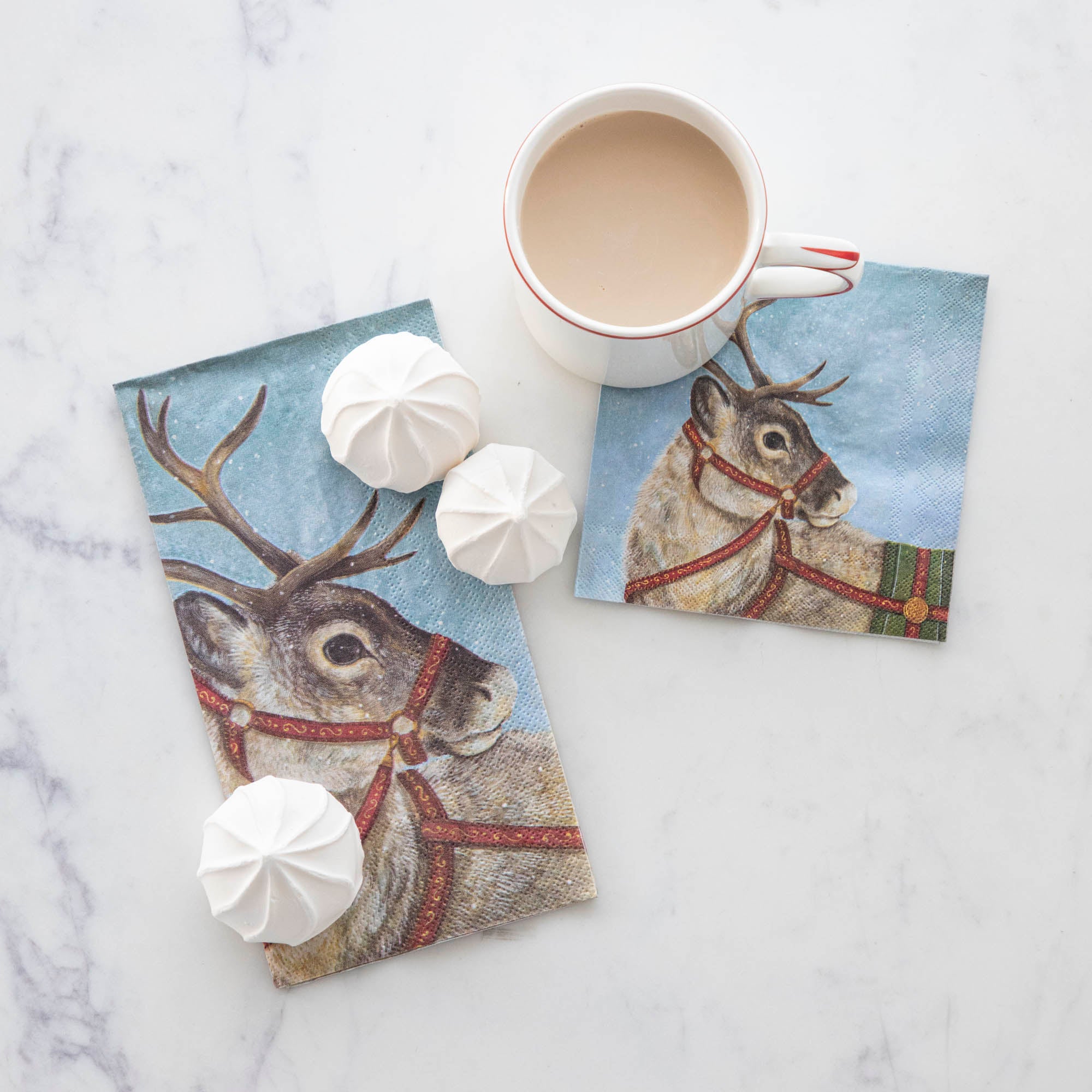 A Dashing Reindeer Guest and Cocktail Napkin on a table with holiday treats and a cup of hot cocoa.