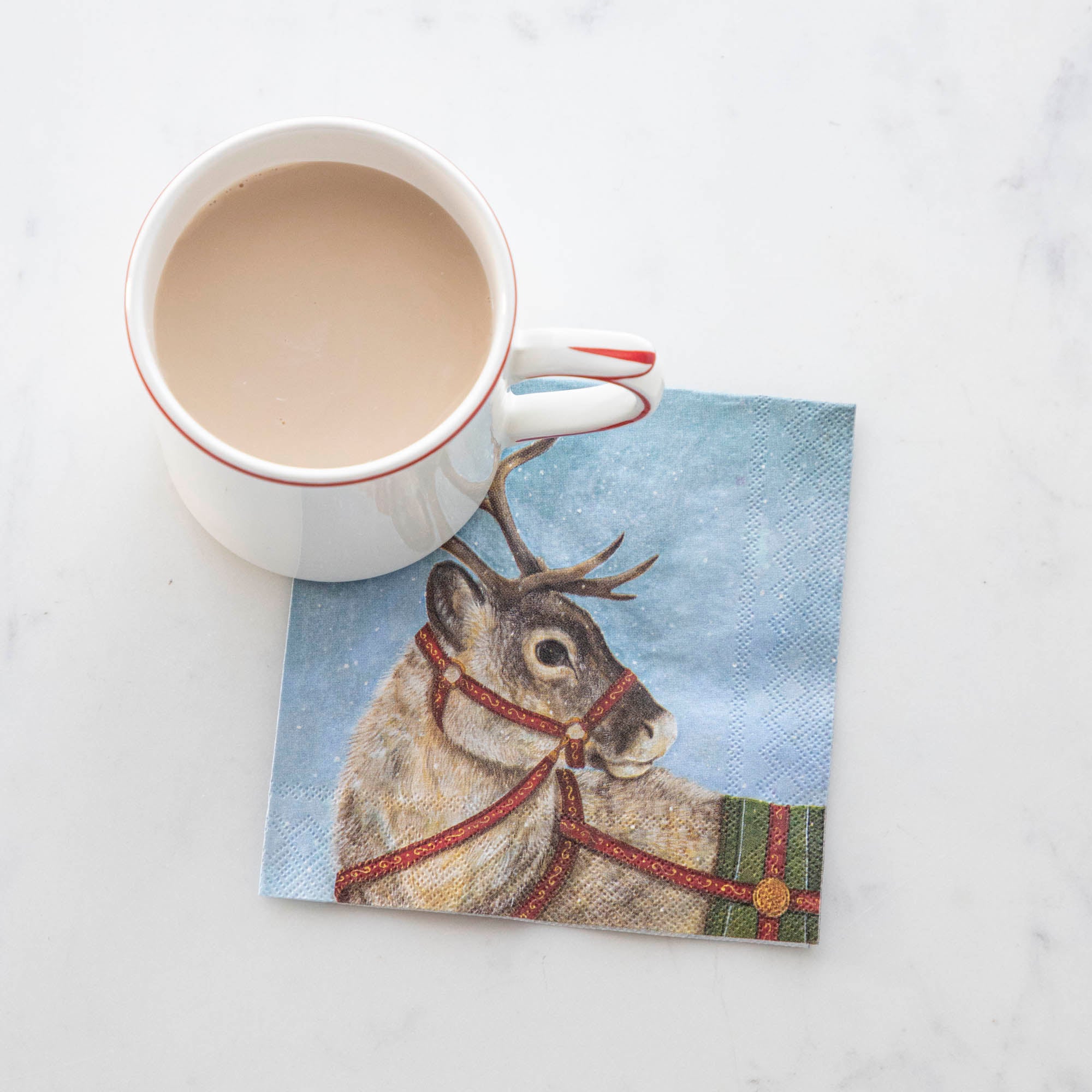 A Dashing Reindeer Cocktail Napkin under a cup of hot cocoa.
