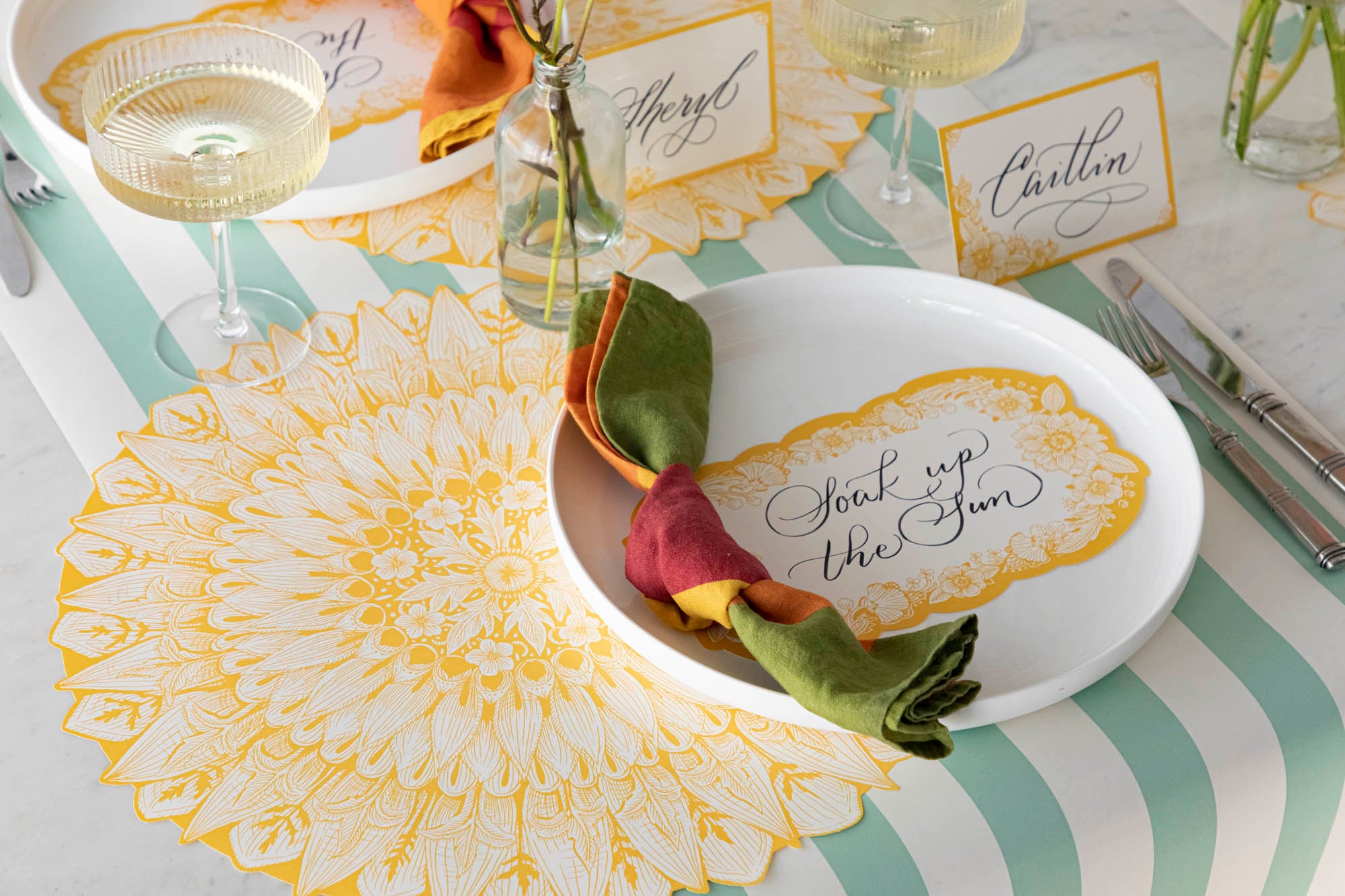 A Spring Blooms Table Card with "Soak up the sun" written on it in lovely script resting on the plate of a vibrant place setting.
