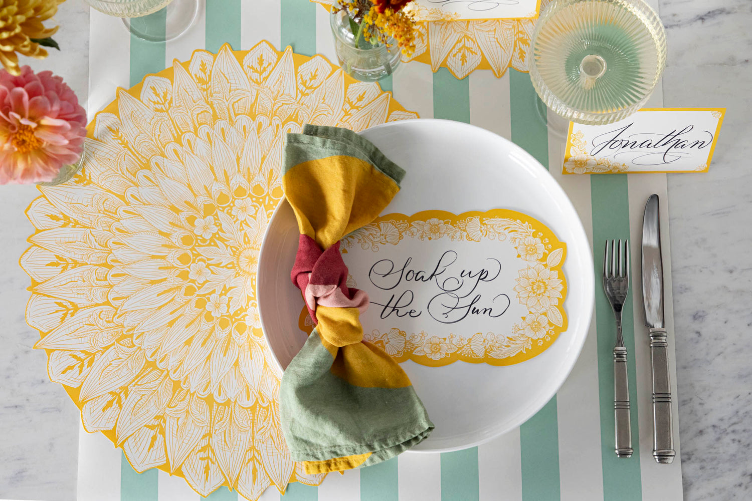 Close-up of a Spring Blooms Table Card with &quot;Soak up the sun&quot; written on it in lovely script resting on the plate of a vibrant place setting.