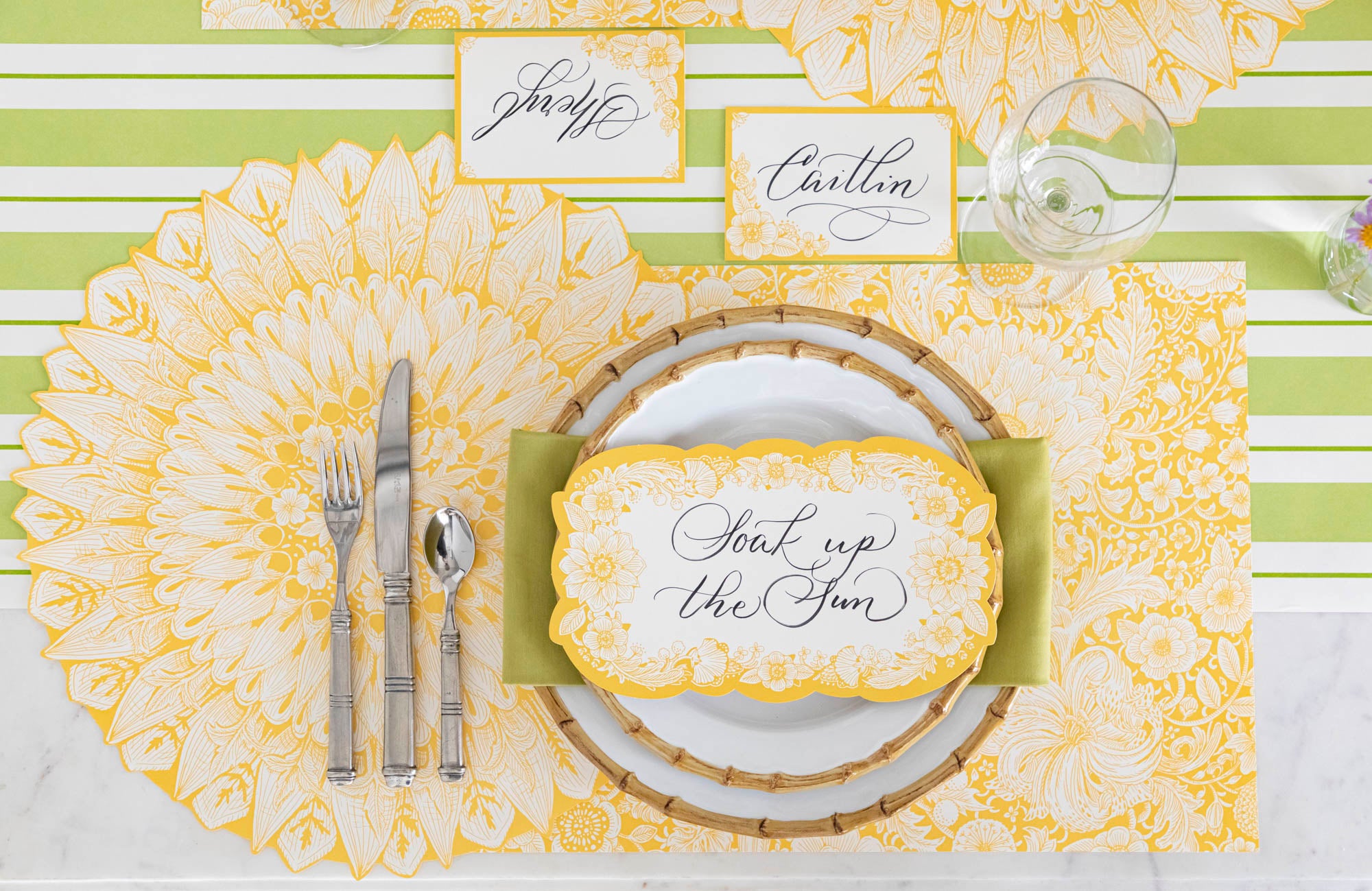 Top-down view of a vibrant floral place setting featuring a Spring Blooms Place Card labeled &quot;Caitlin&quot; laying flat on the table behind the plate.