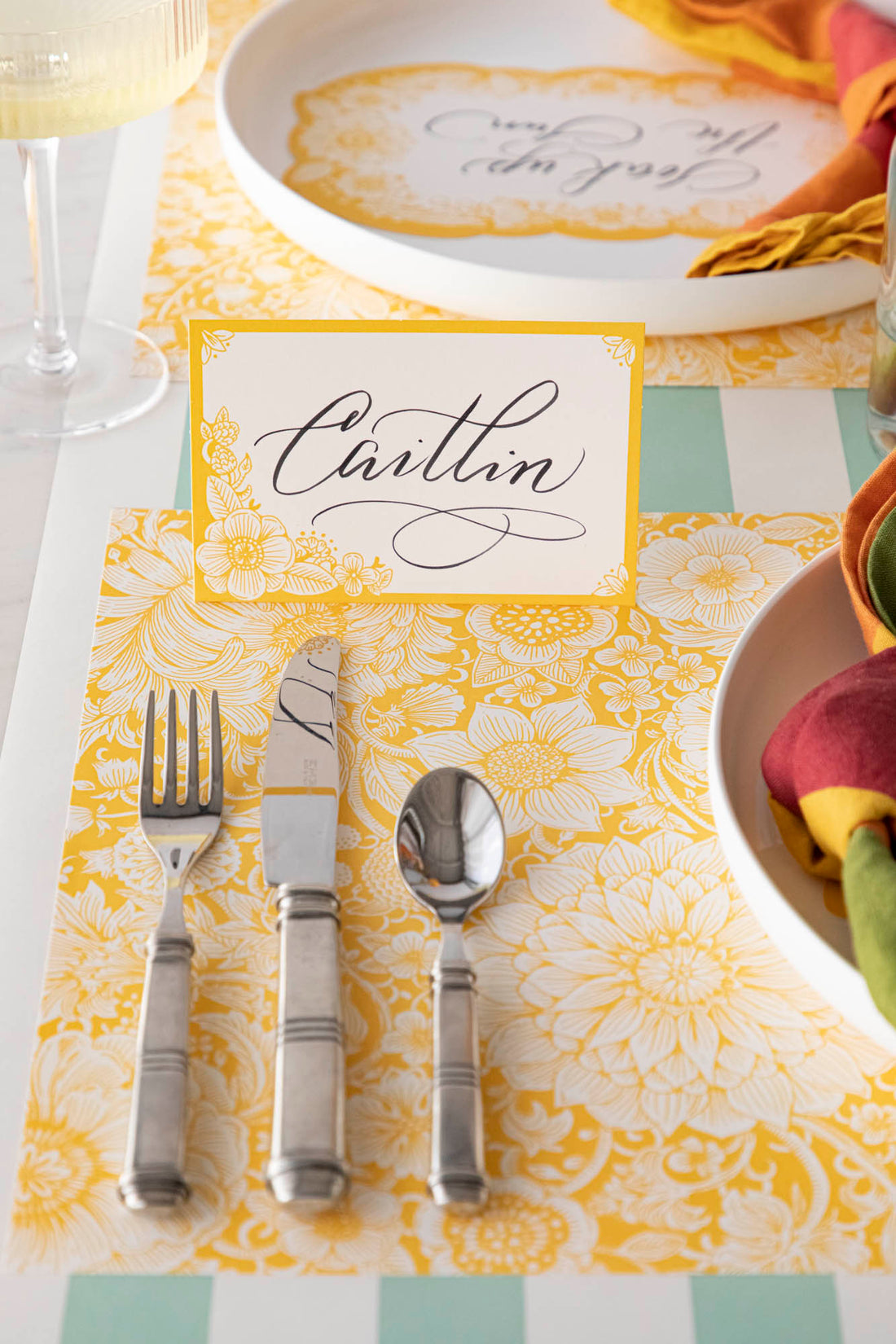 A Spring Blooms Place Card labeled &quot;Caitlin&quot; standing at an elegant floral place setting.