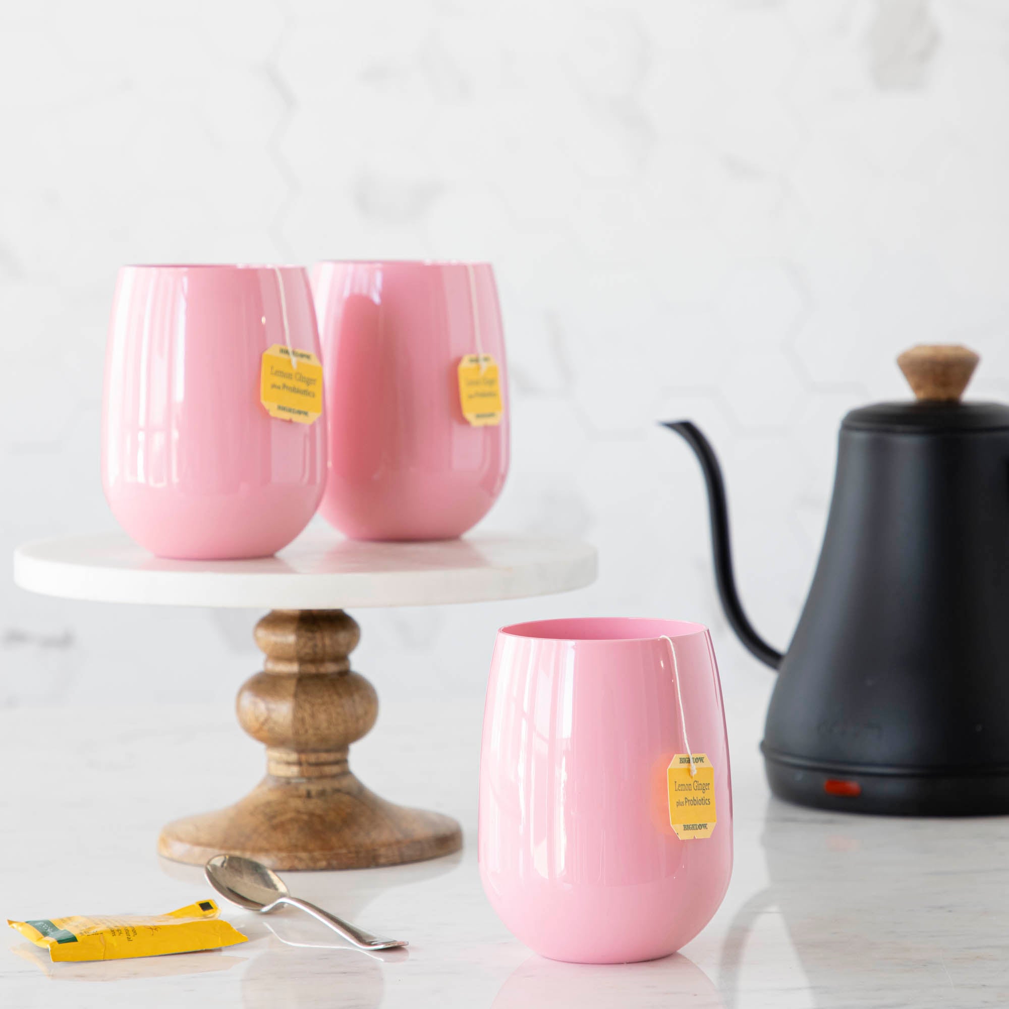 3 Pink SymGlasses with tea bags coming out of them and a tea kettle in the background.