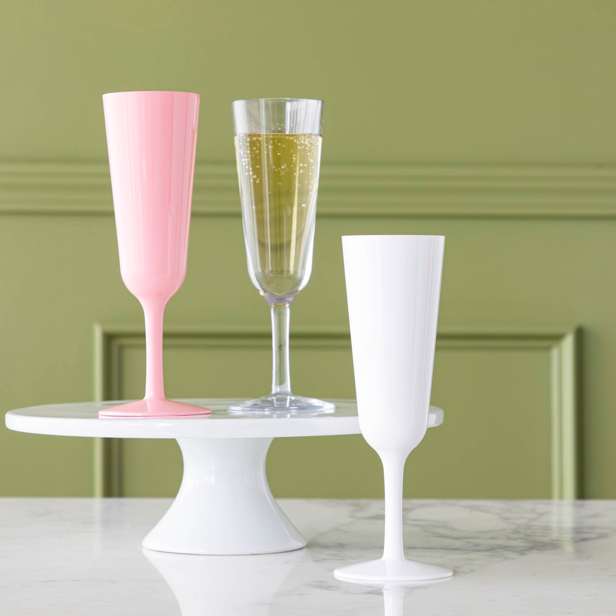Three symGlass champagne glasses in pink, clear and white on a marble table.