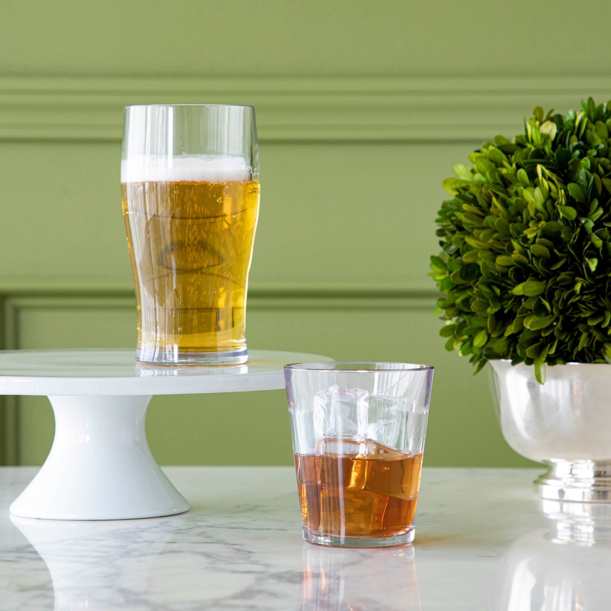 A clear tulip symGlass and a clear rocks symGlass with beverages on a marble table.