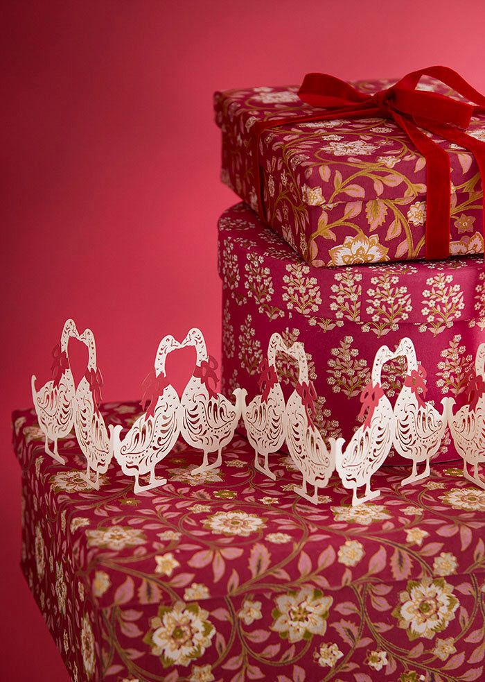 Decorative gift boxes with floral patterns and white paper geese on a red background.