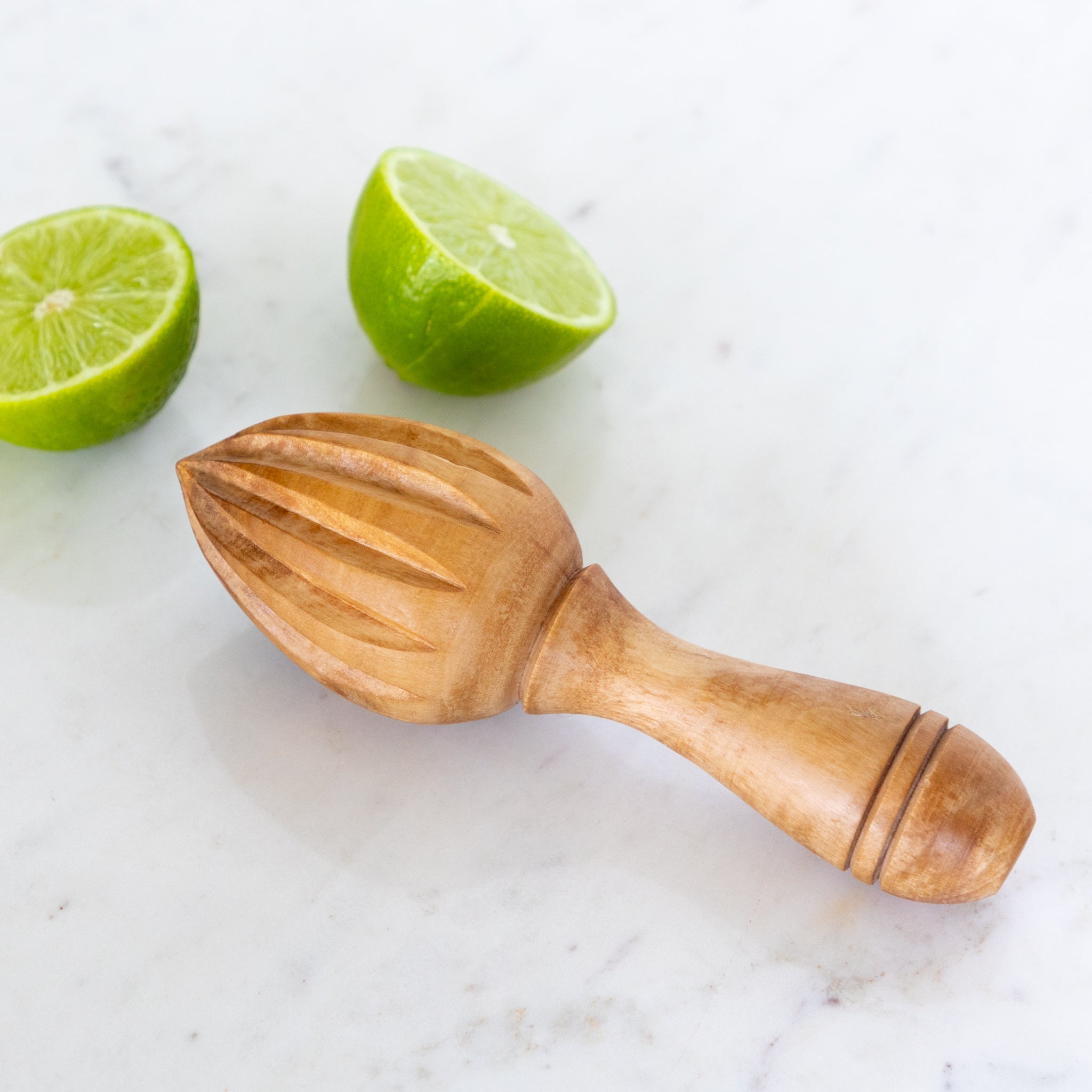 Wooden juicer with two limes on a marble surface.