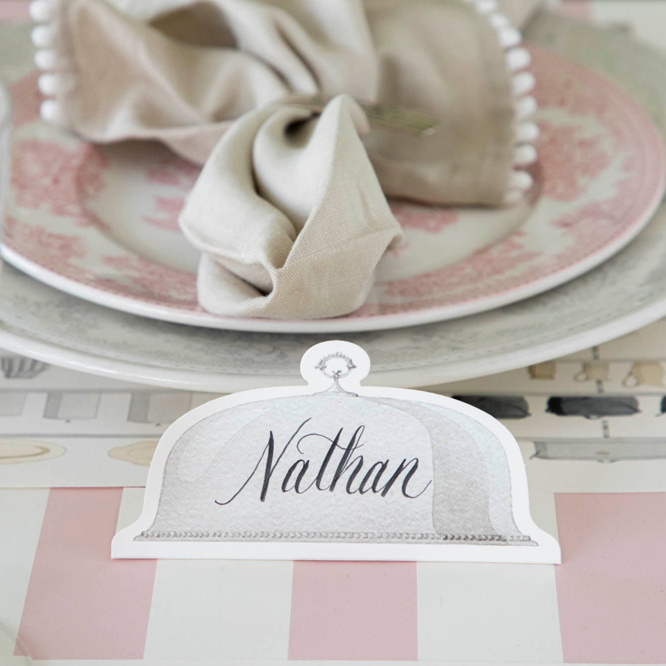 Serving Dome Place Card with "Nathan" written on it, in front of a place setting.