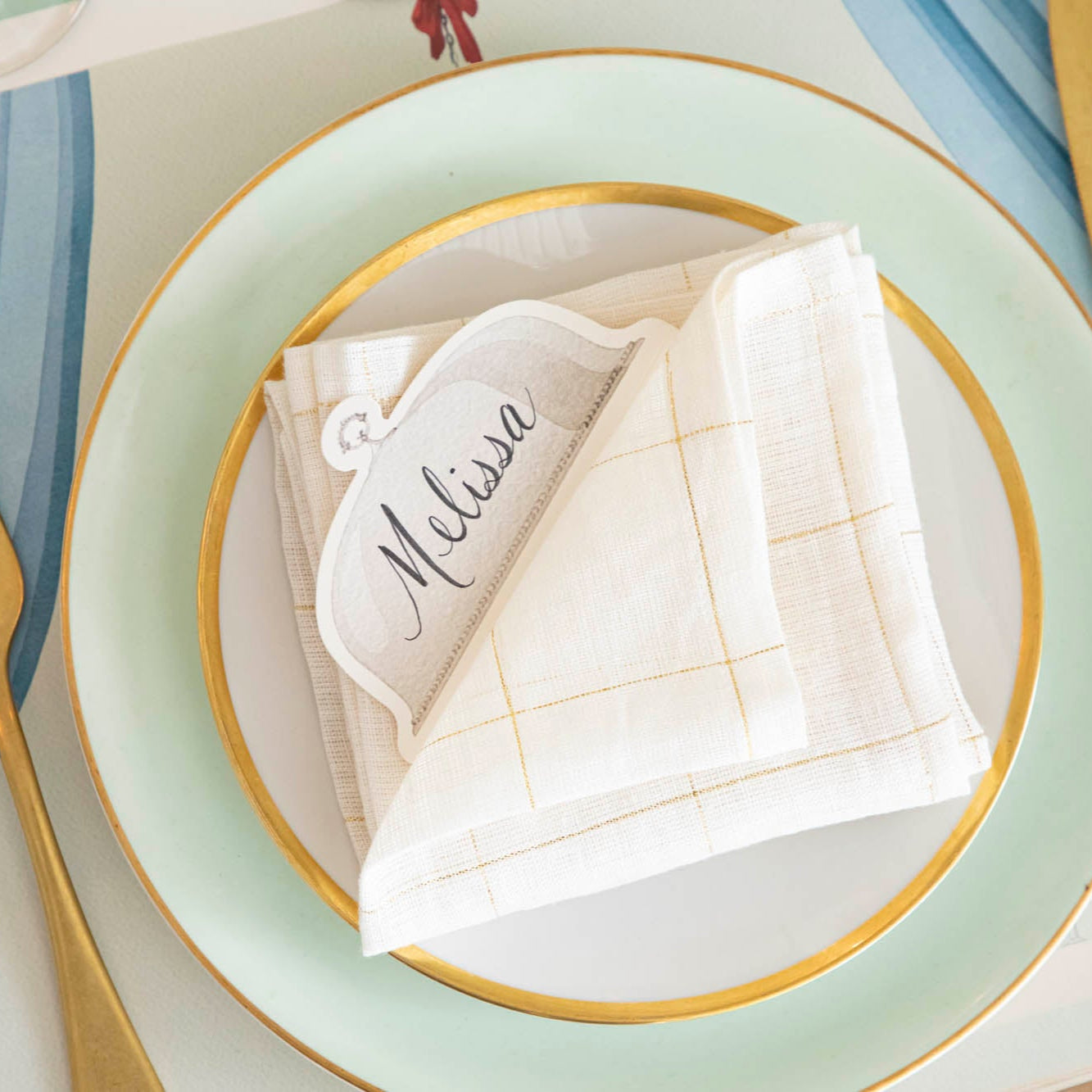 Serving Dome Place Card with "Melissa" written on it, resting on a folded napkin, on top of dinner plates.