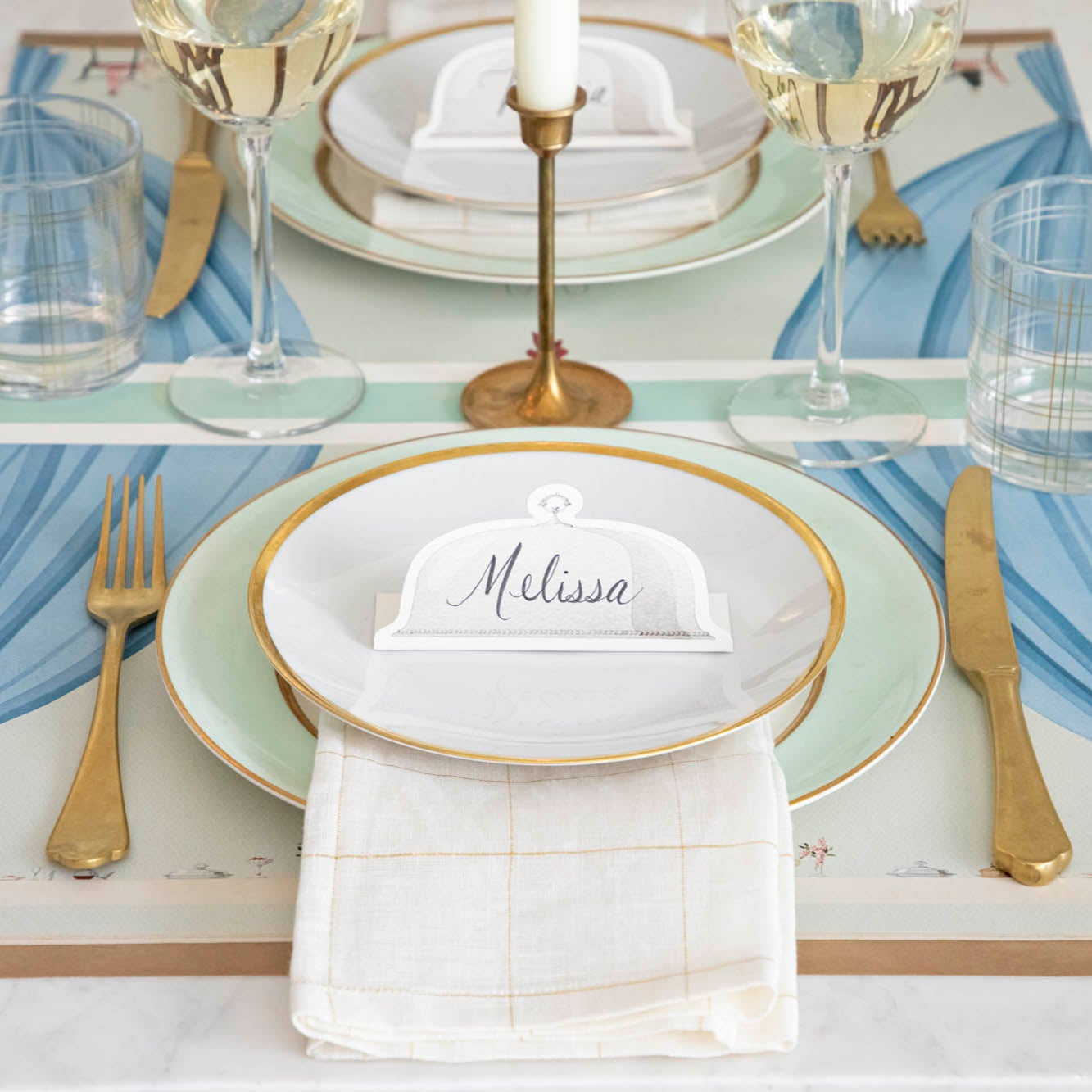 Serving Dome Place Card with "Melissa" written on it, resting on dinner plates on an elegant place setting.
