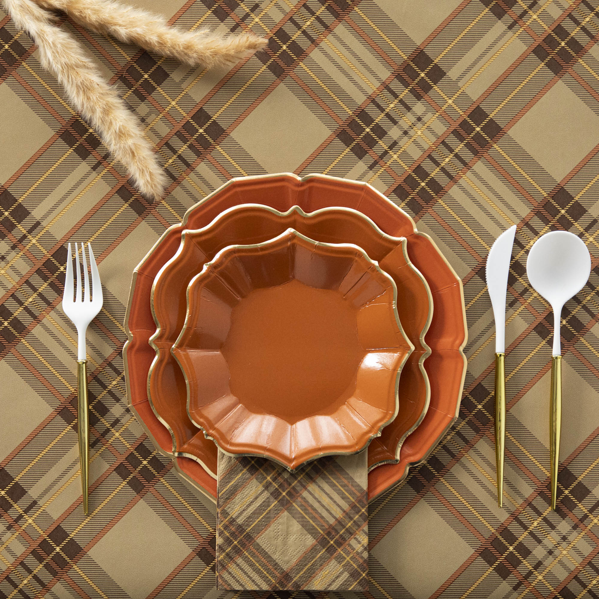 A set of orange scalloped plates with gold rims on a plaid background, accompanied by white utensils with gold accents.