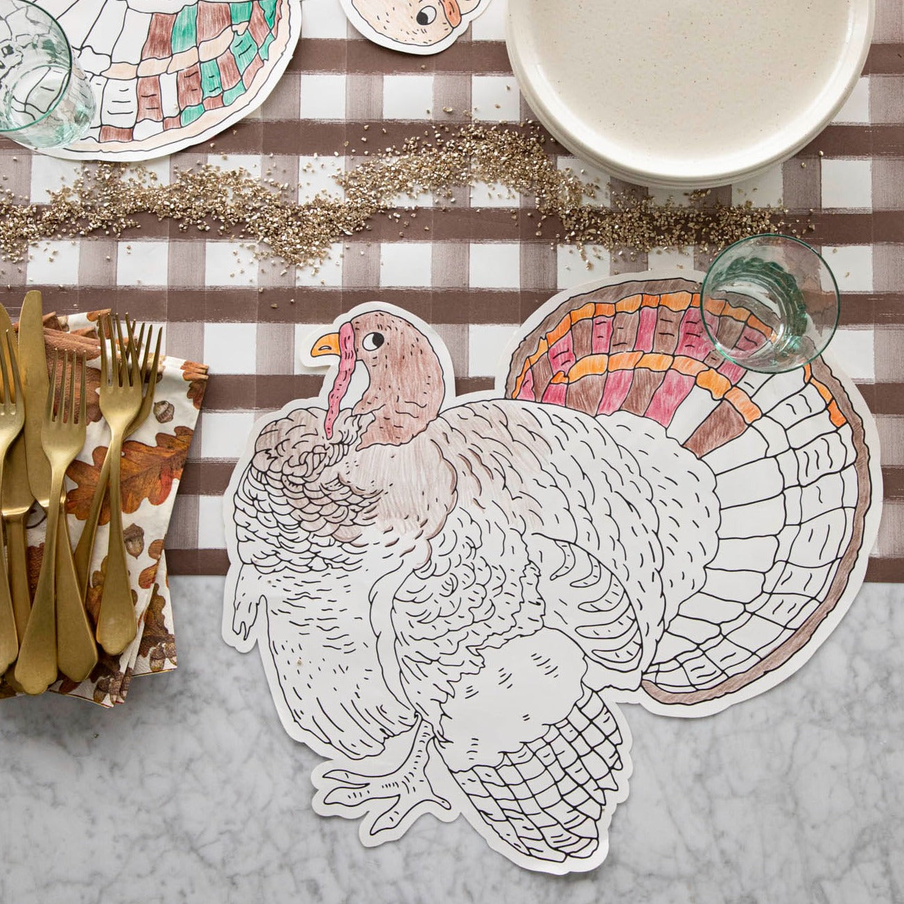 Die-cut coloring turkey placemat partially colored in with 2 colored pencils laying atop it on a brown painted check runner.