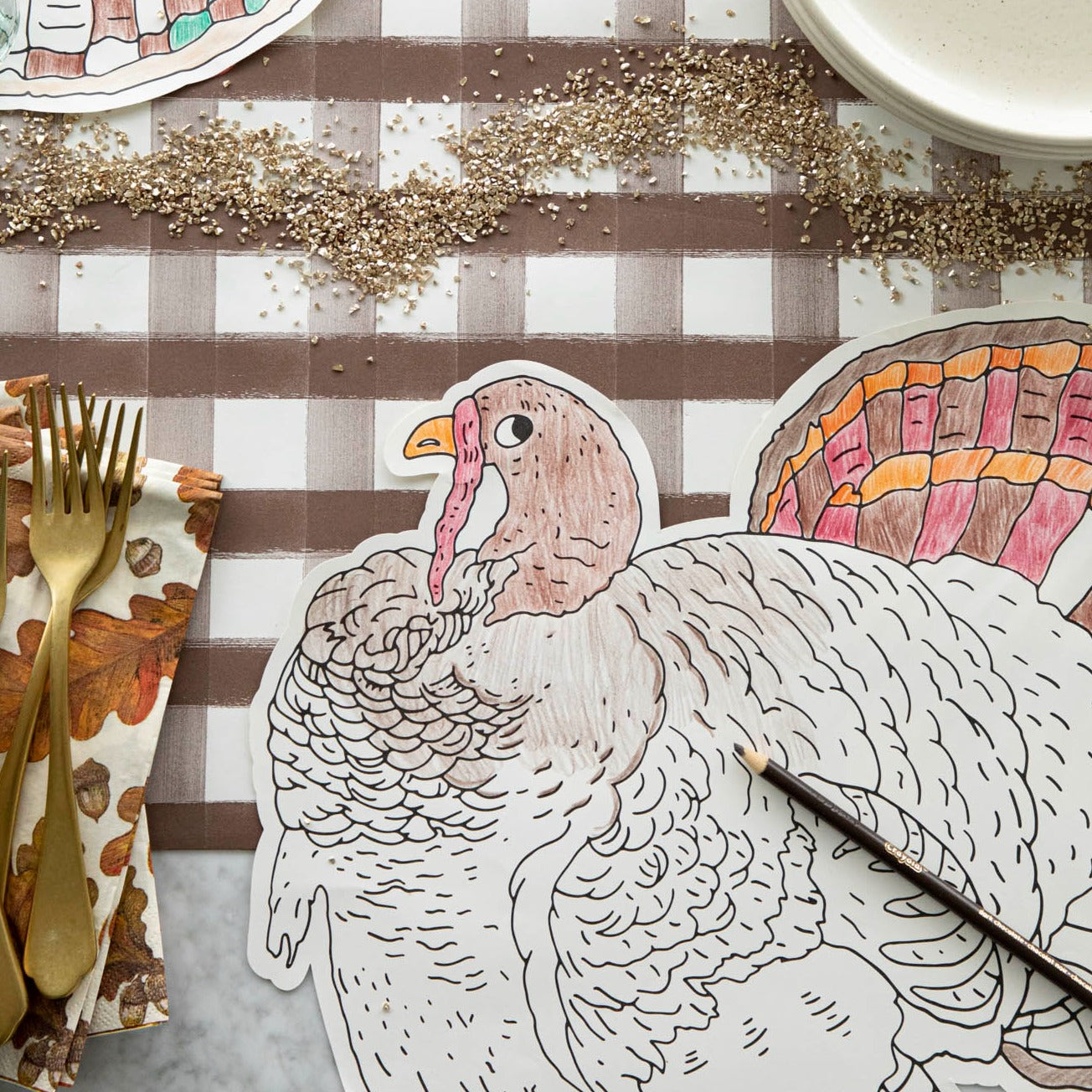 Die-cut coloring turkey placemat partially colored in with 2 colored pencils laying atop it on a green stripe runner.