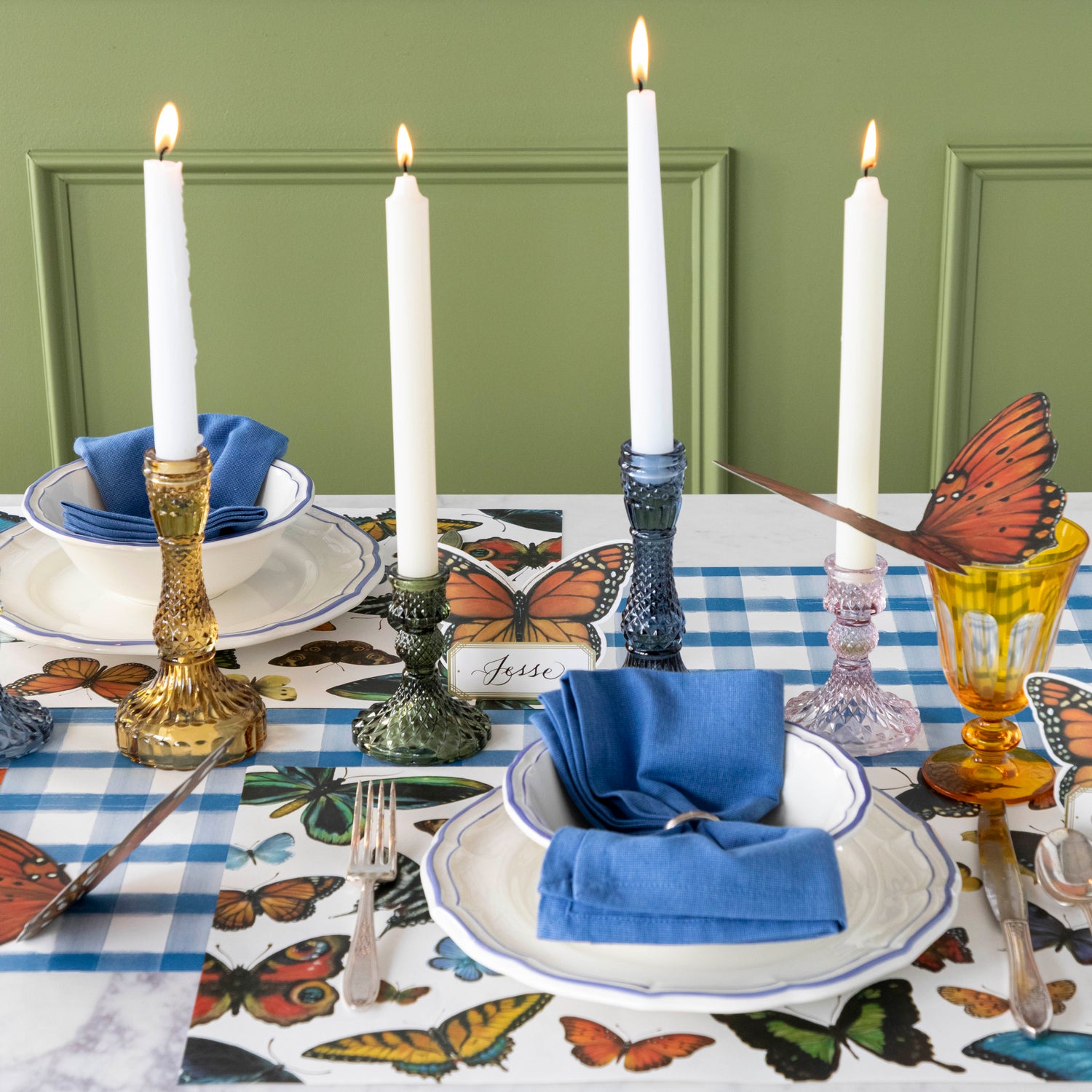 A set of four glass candle holders, yellow, green, blue and pink on a set table.