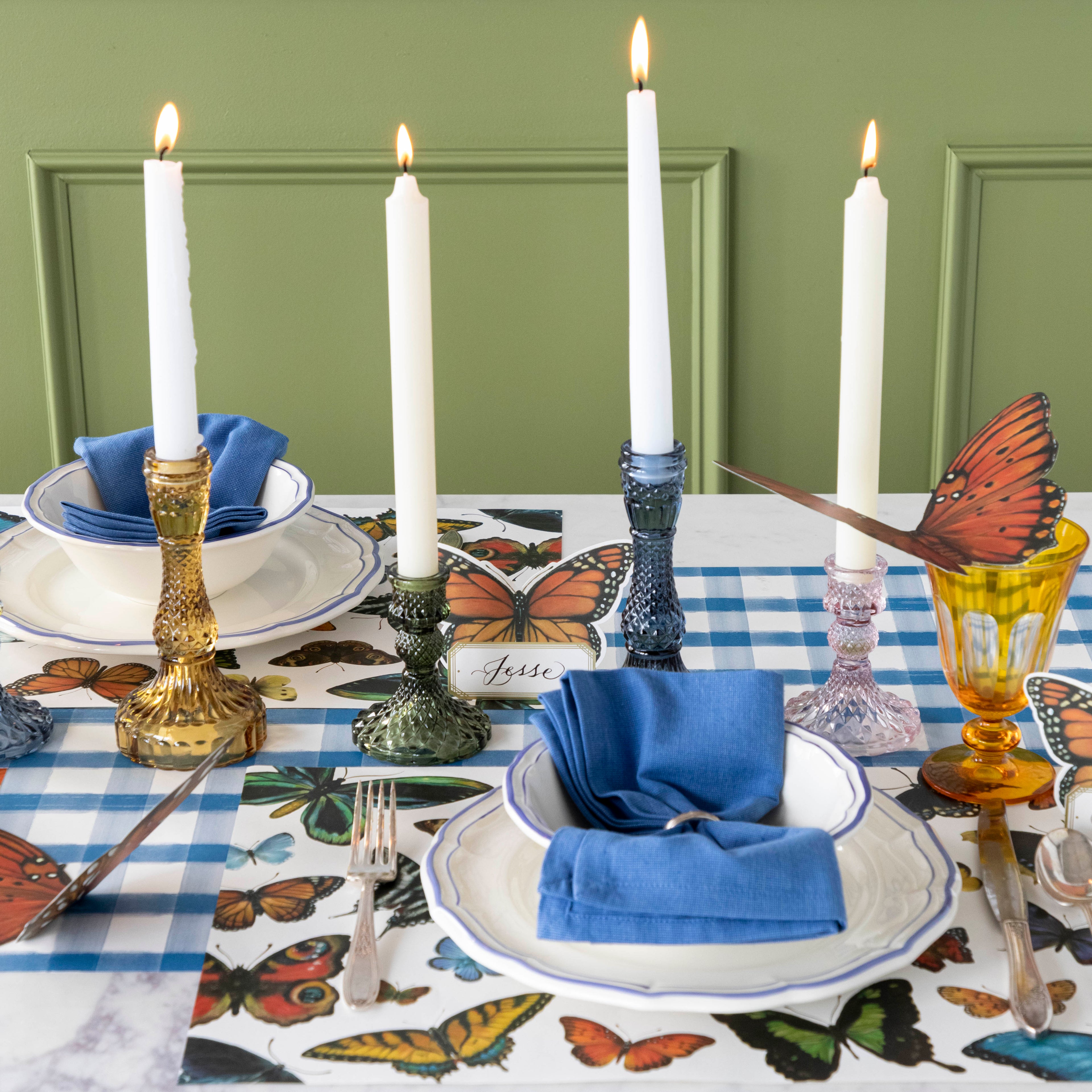 A set of four glass candle holders, yellow, green, blue and pink on a set table.