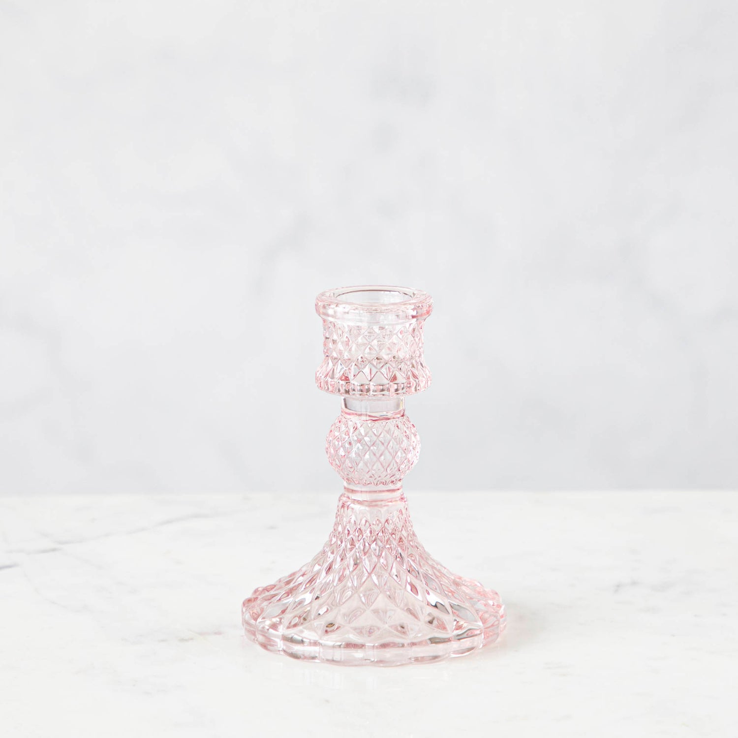 A pink glass candlestick on a white background.