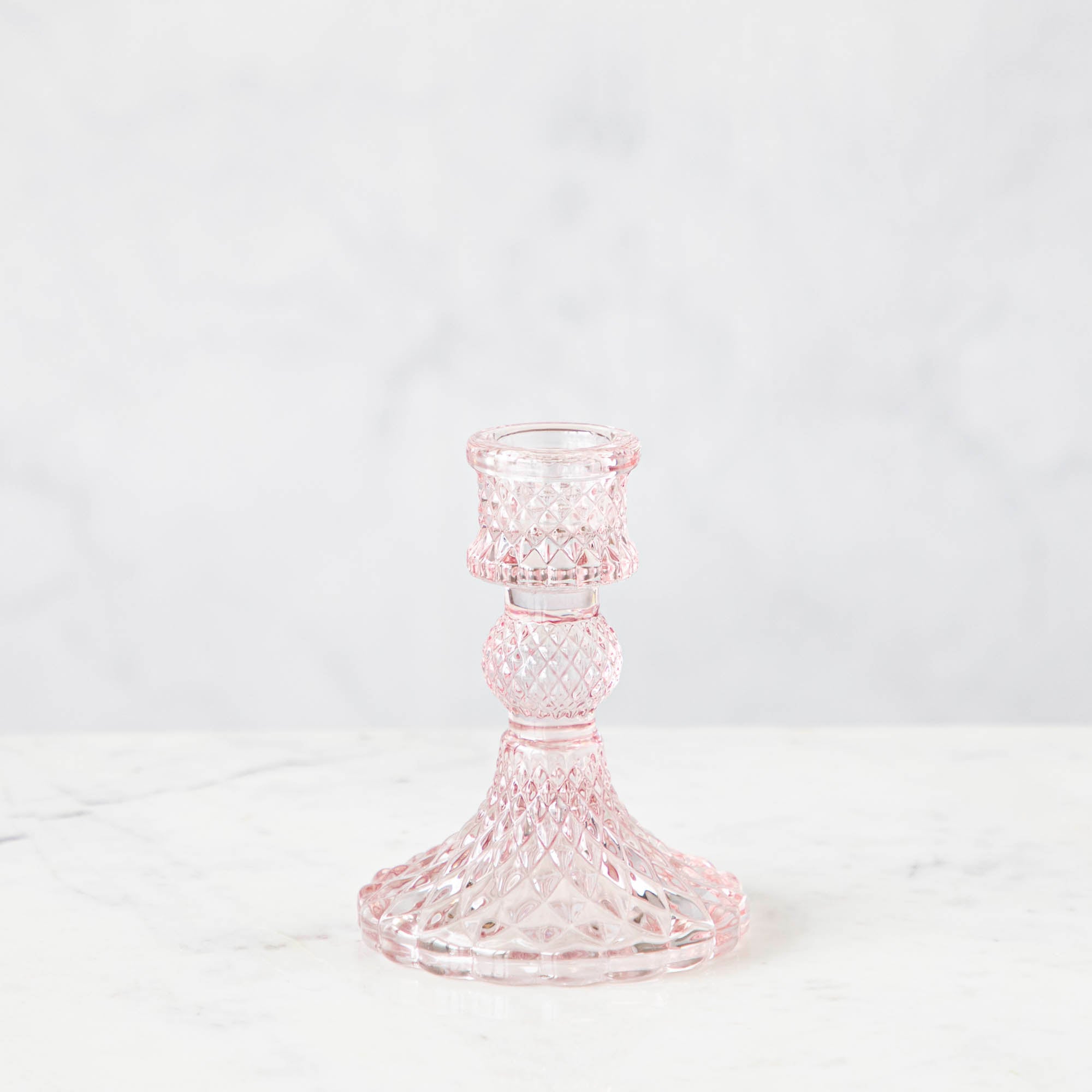 A pink glass candlestick on a white background.