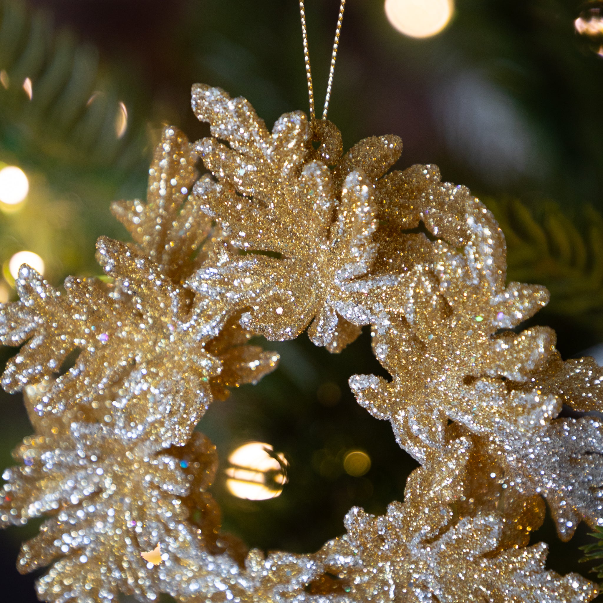 Decorative gold wreath ornament on a Christmas tree with blurred lights in the background.
