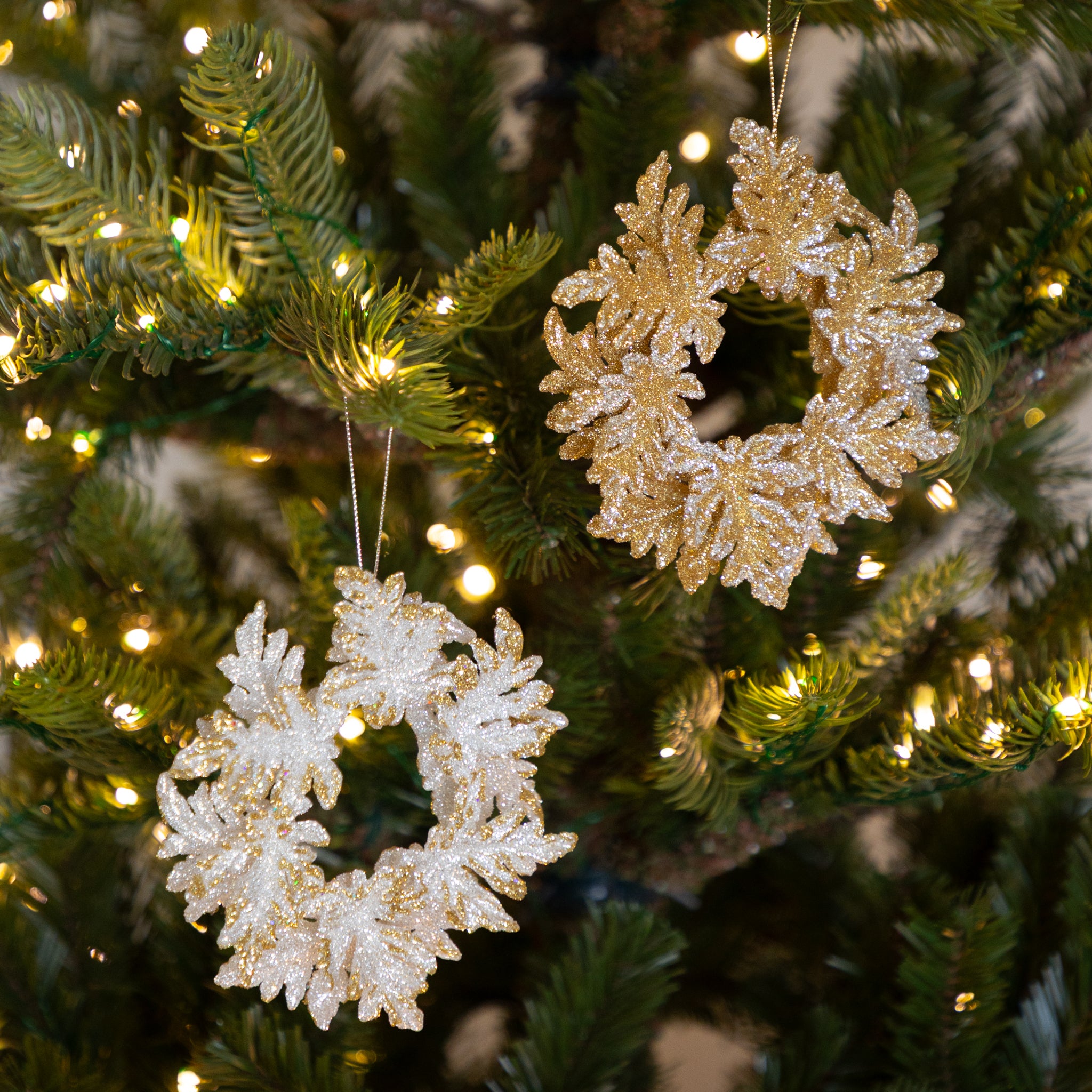 Decorative gold and silver wreath ornaments on a Christmas tree with lights.