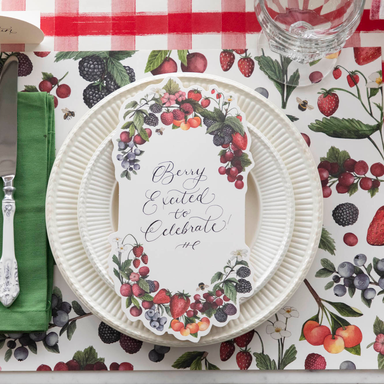Top-down view of a berry-themed place setting featuring a Berry Bramble Table Card with "Berry Excited to Celebrate" written on it in lovely script.