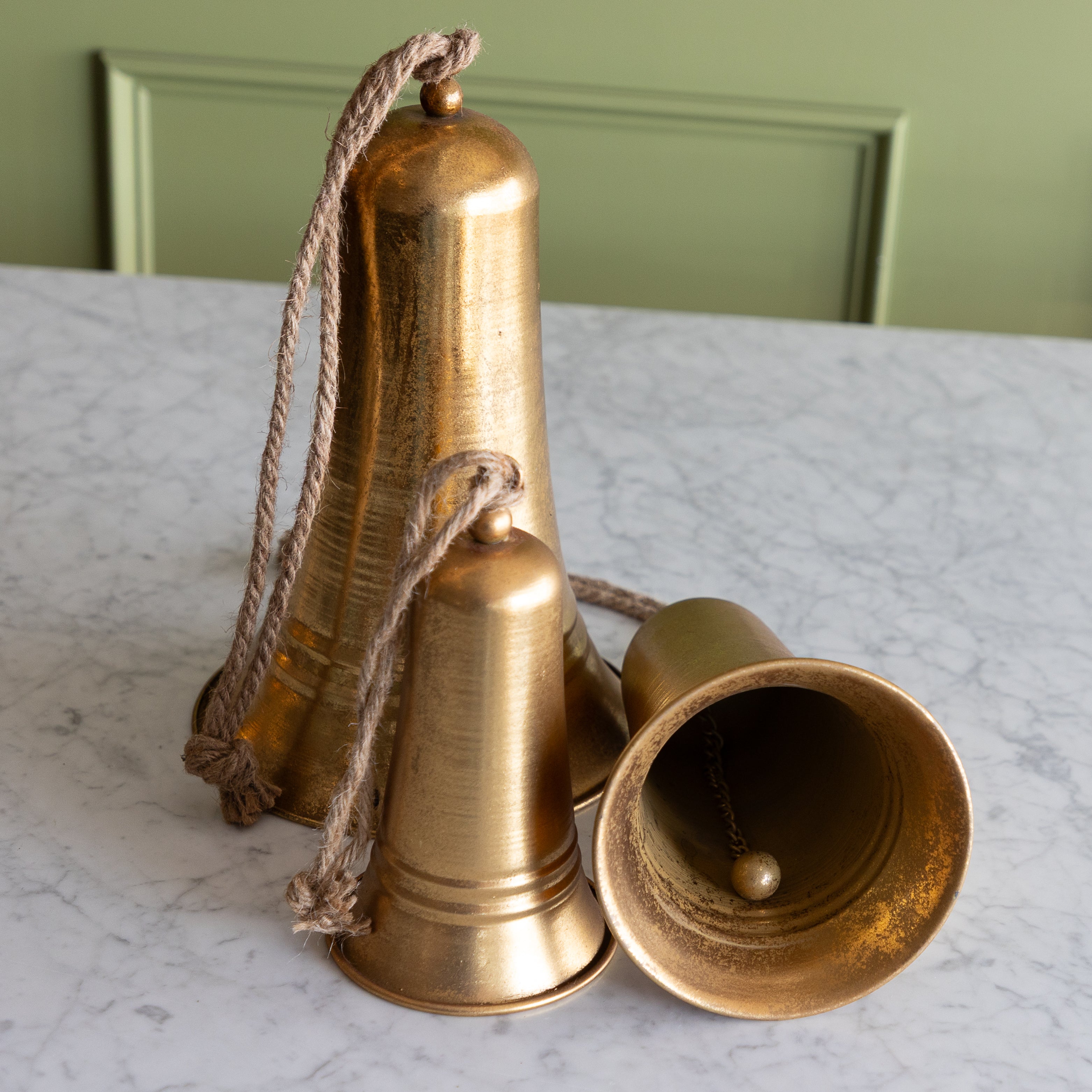 Three brass bells on a marble surface with a green panel background