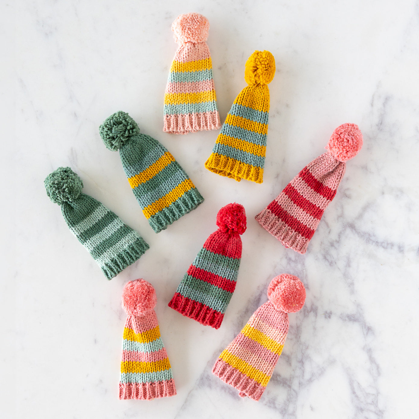 Colorful knitted hats with pom-poms on a marble surface.