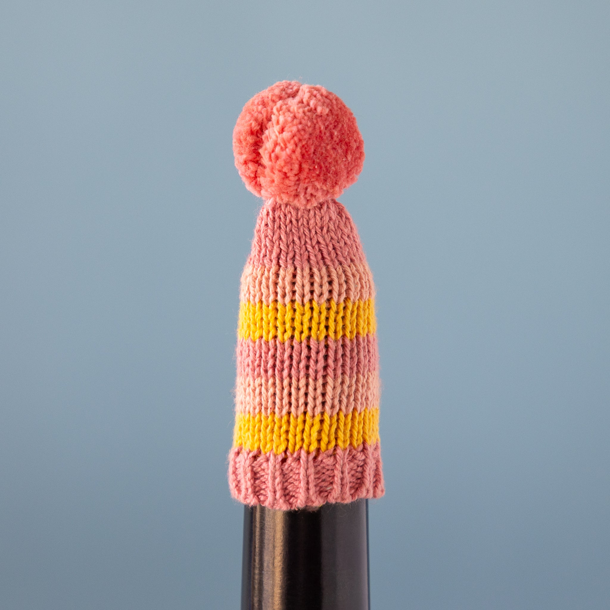 Knitted hat with a pink and yellow pattern on a gray background on a dark bottle.
