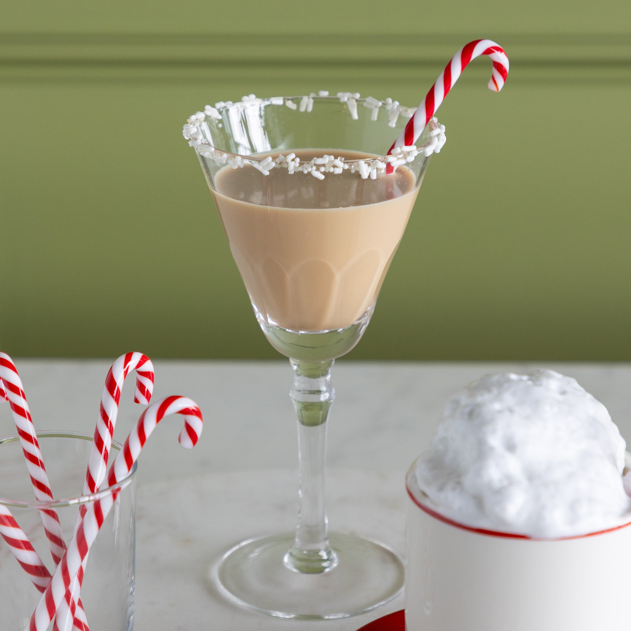 Mocha cocktail in a martini glass with a candy cane stir stick on a white surface.