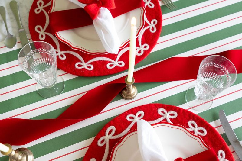 A holiday table setting with a loosely twisted red ribbon running down the center of the table.
