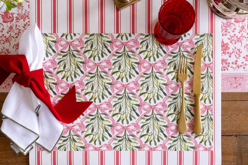 A holiday tablescape featuring the mistletoe placemat on a red and white striped runner.
