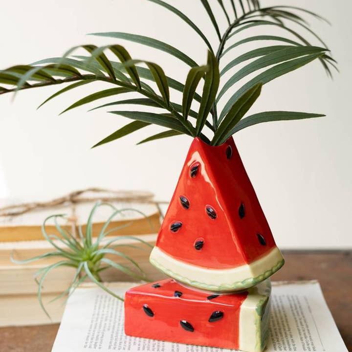 Watermelon-shaped ceramic vase with green plant on a wooden surface