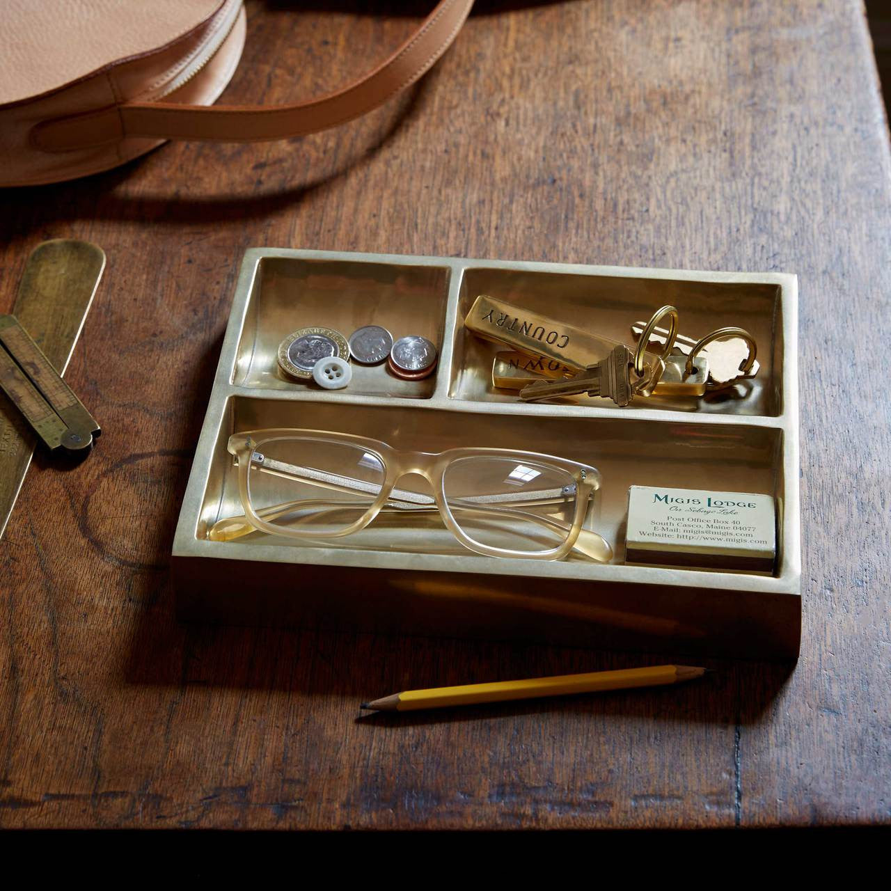 Brass catchall tray with various change, keys and glasses in it.