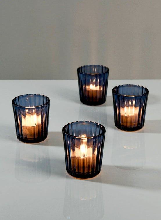 Four navy blue glass candle holders with lit candles on a white surface.