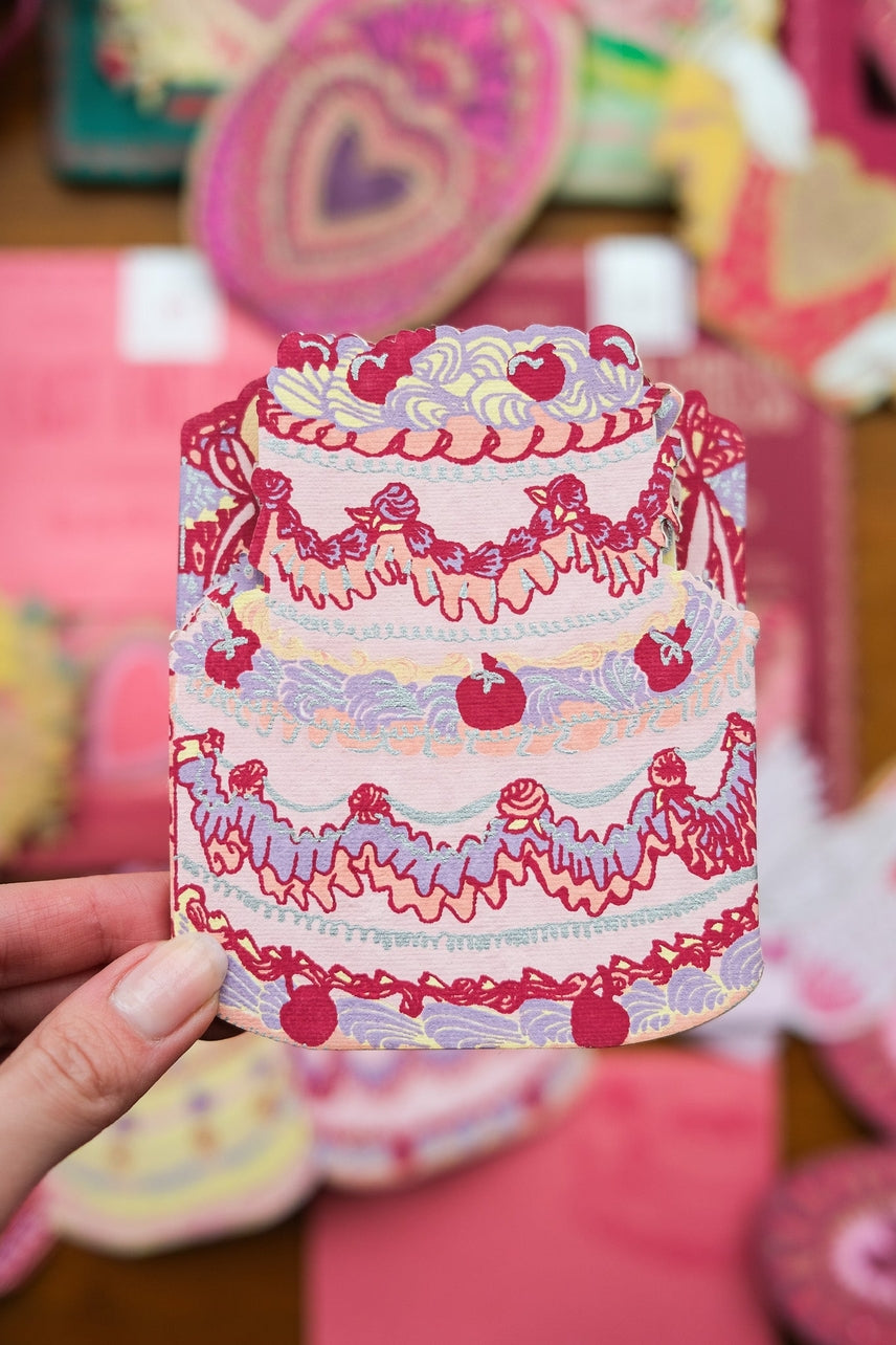 Decorative card with a cake design held by a hand.