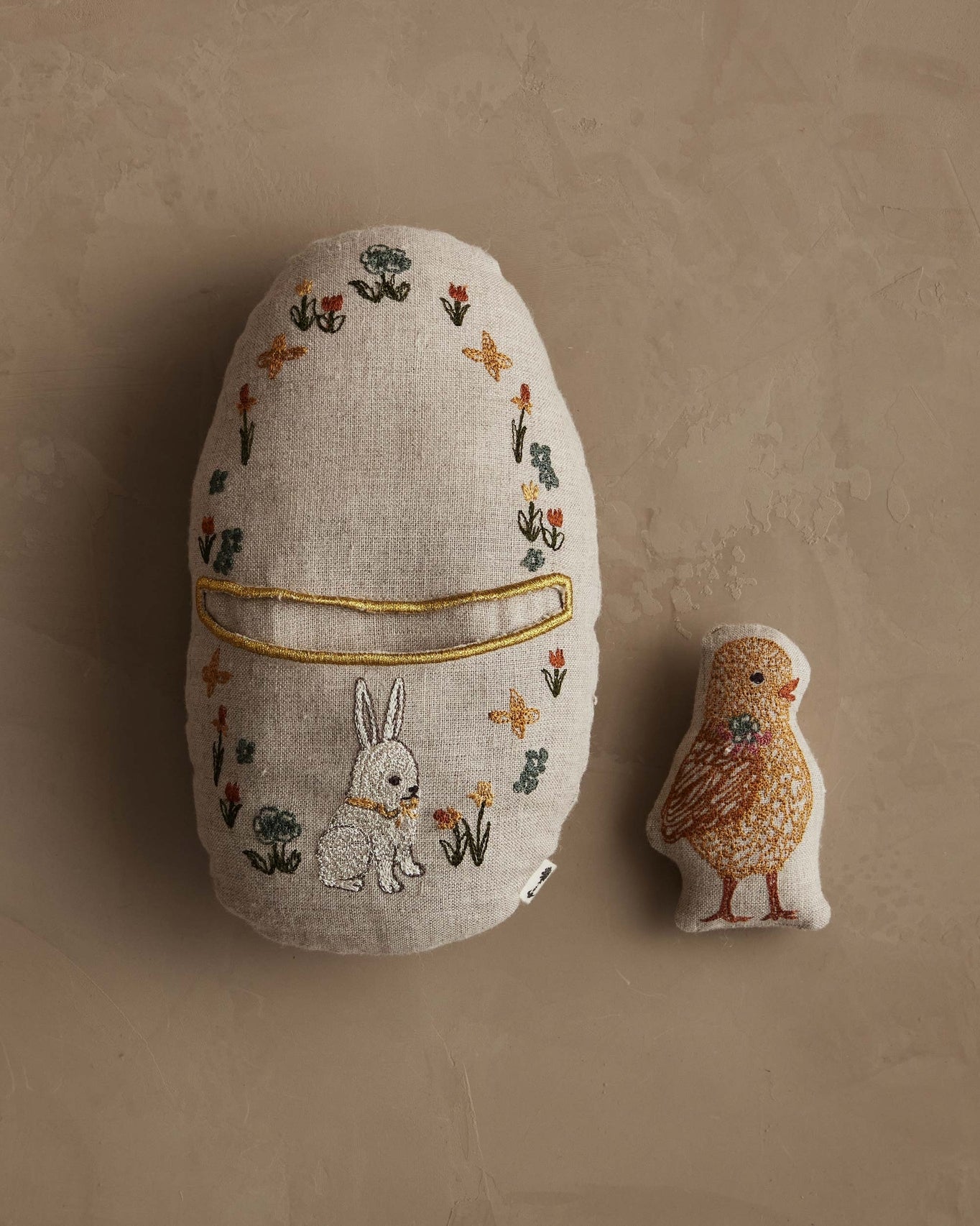 Decorative egg-shaped pillow with embroidered design on a beige background.