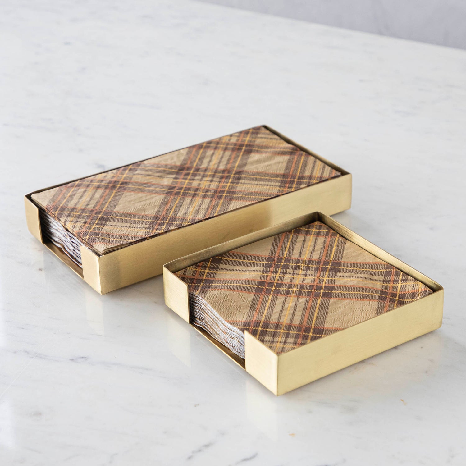 Two Brass Napkin Holders, guest-sized and cocktail-sized, containing brown plaid napkins on a white table.