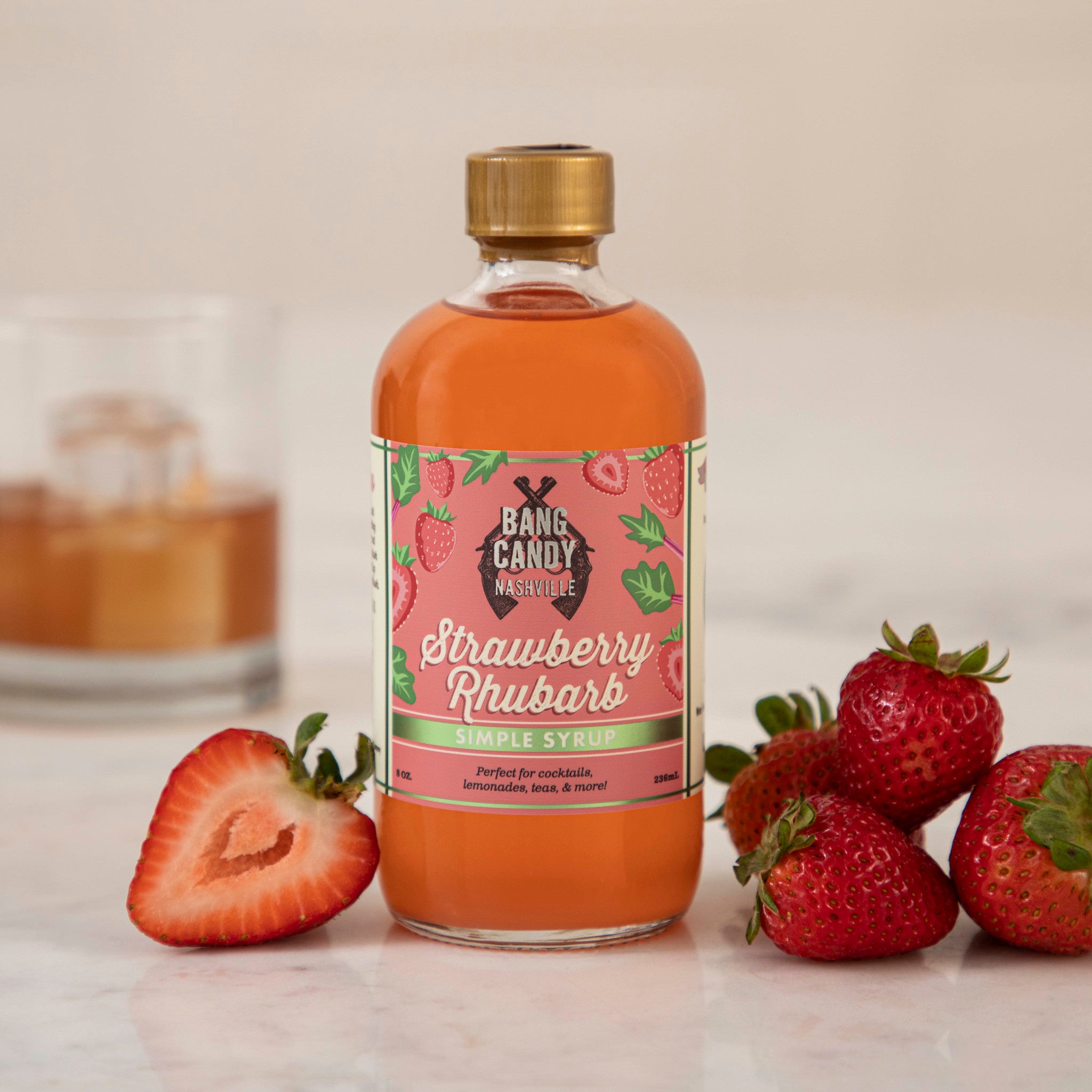 A bottle of Hester & Cook Strawberry Rhubarb Syrup with strawberries next to it, perfect for creating refreshing Pimms Cup cocktails or summer sodas.
