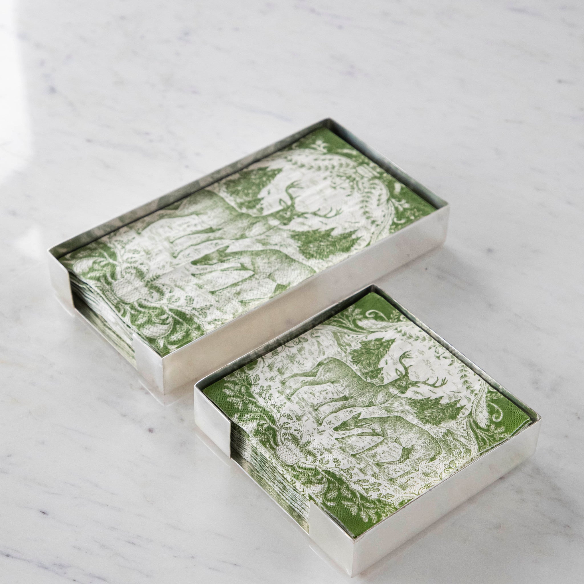 Two Silver Napkin Holders, guest-sized and cocktail-sized, containing green and white napkins on a white table.