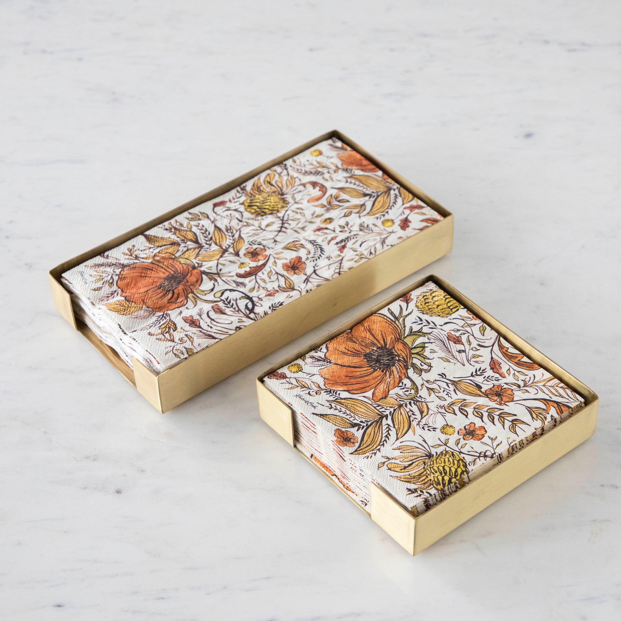 Two Brass Napkin Holders, guest-sized and cocktail-sized, containing autumnal napkins on a white table.