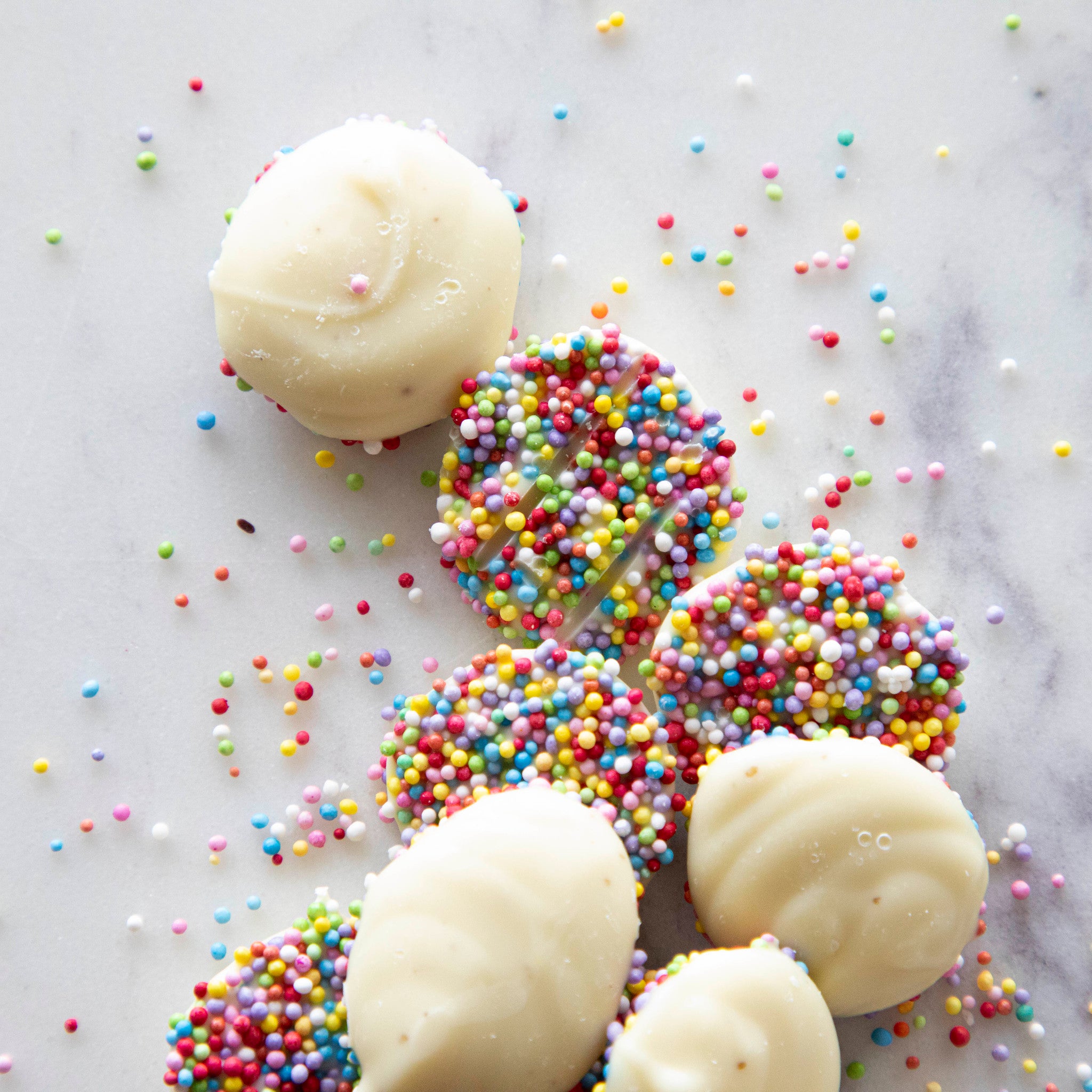 White cookies with sprinkles and Hester & Cook chocolate buttons on a marble table.