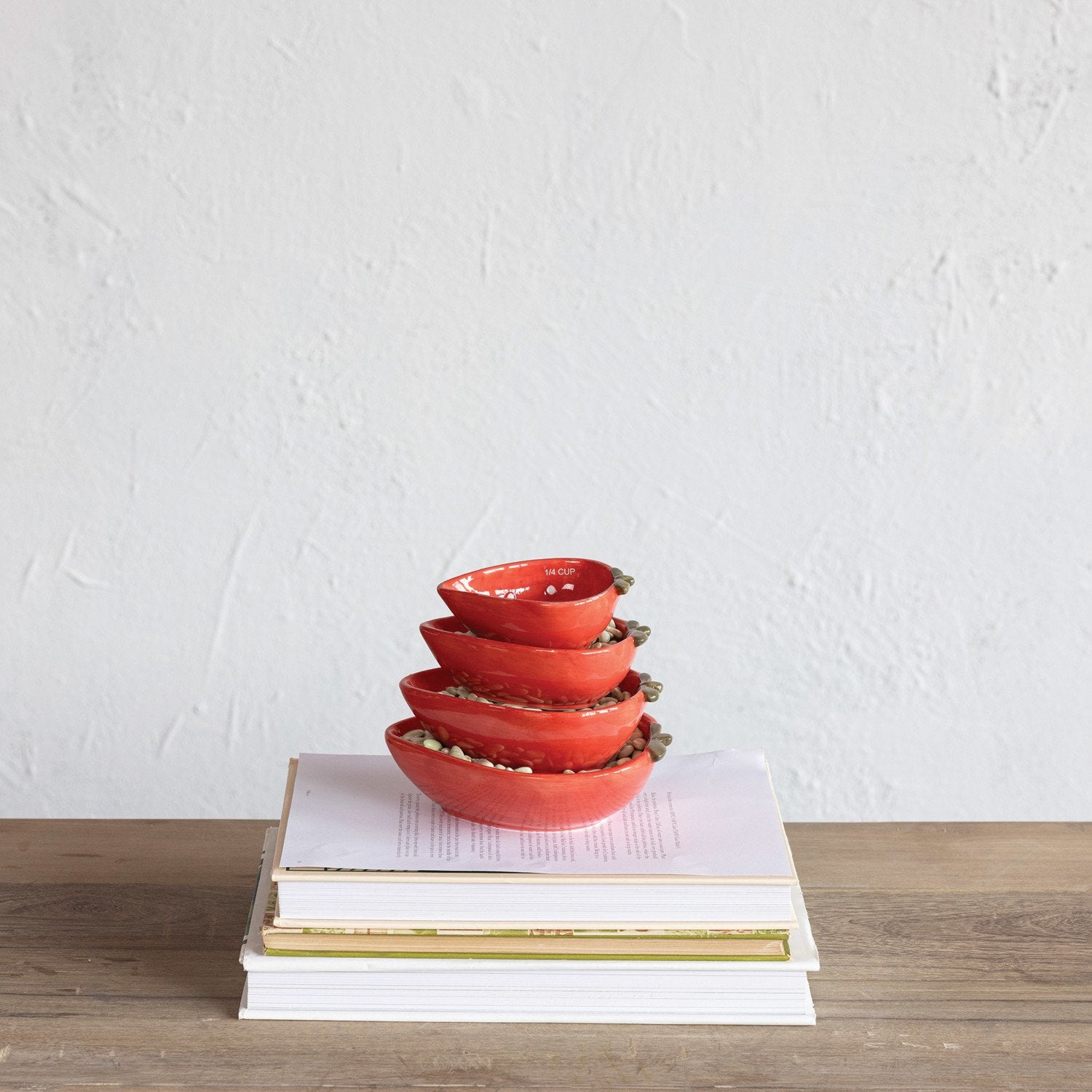 Set of red strawberry shaped measuring cups stacked on a stack of books with a white background.