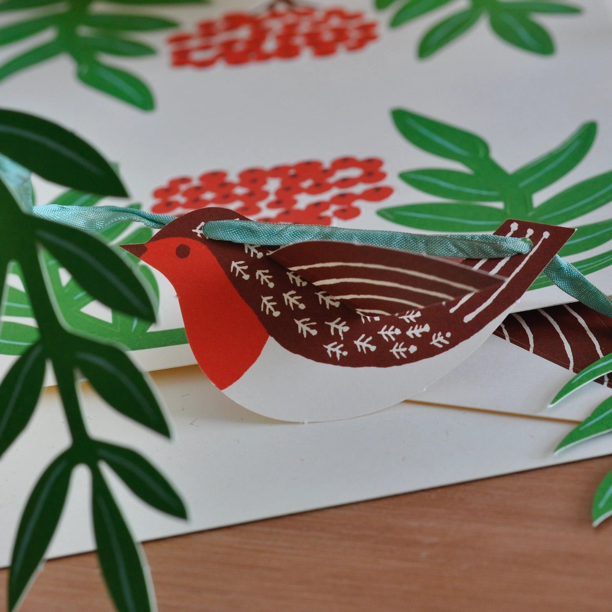 A close-up of the paper robbin with 3D wings, on a green ribbon sitting on a wood table.