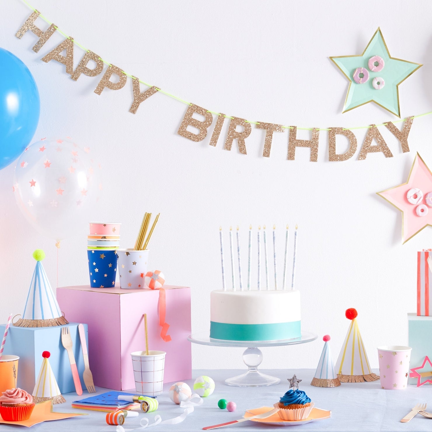 Birthday party setup with cake, balloons, and decorations on a white background
