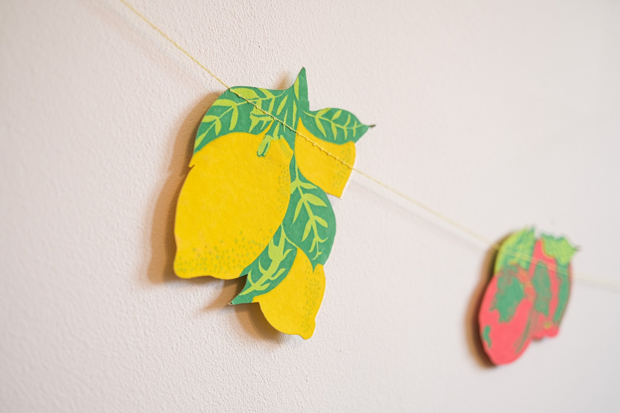 Decorative lemon and strawberry cutouts on a string against a light background.