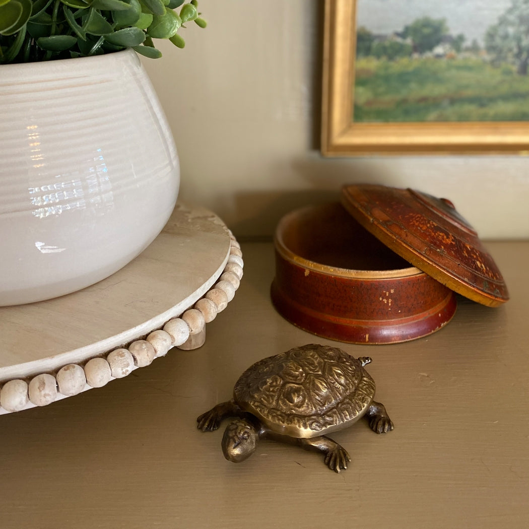 Decorative turtle figurine, brown box, and white pot with plant on a surface.