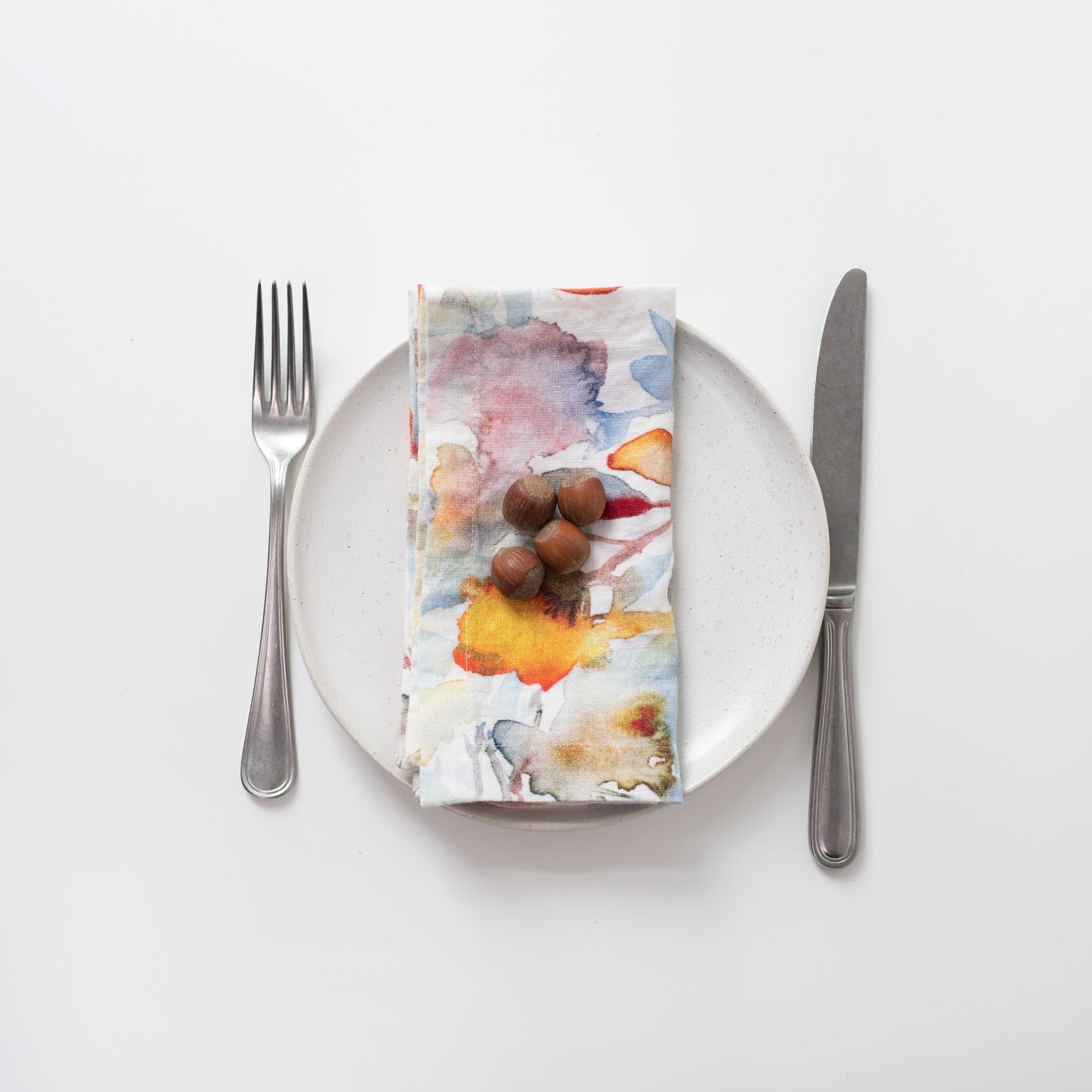 Napkin with a floral design on a white plate with cutlery.