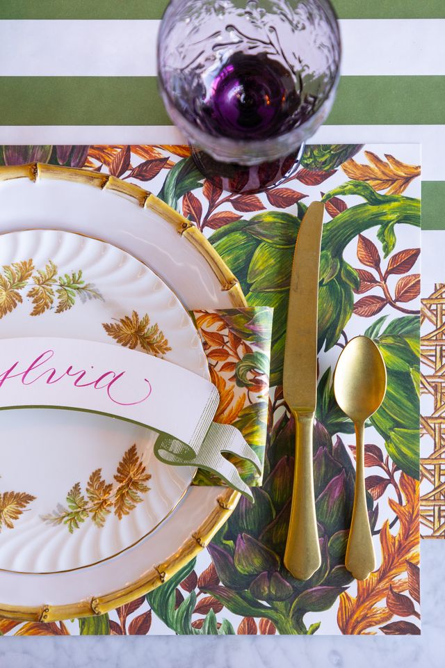 Dining table setting with a leaf-patterned placemat, gold cutlery, and a glass.