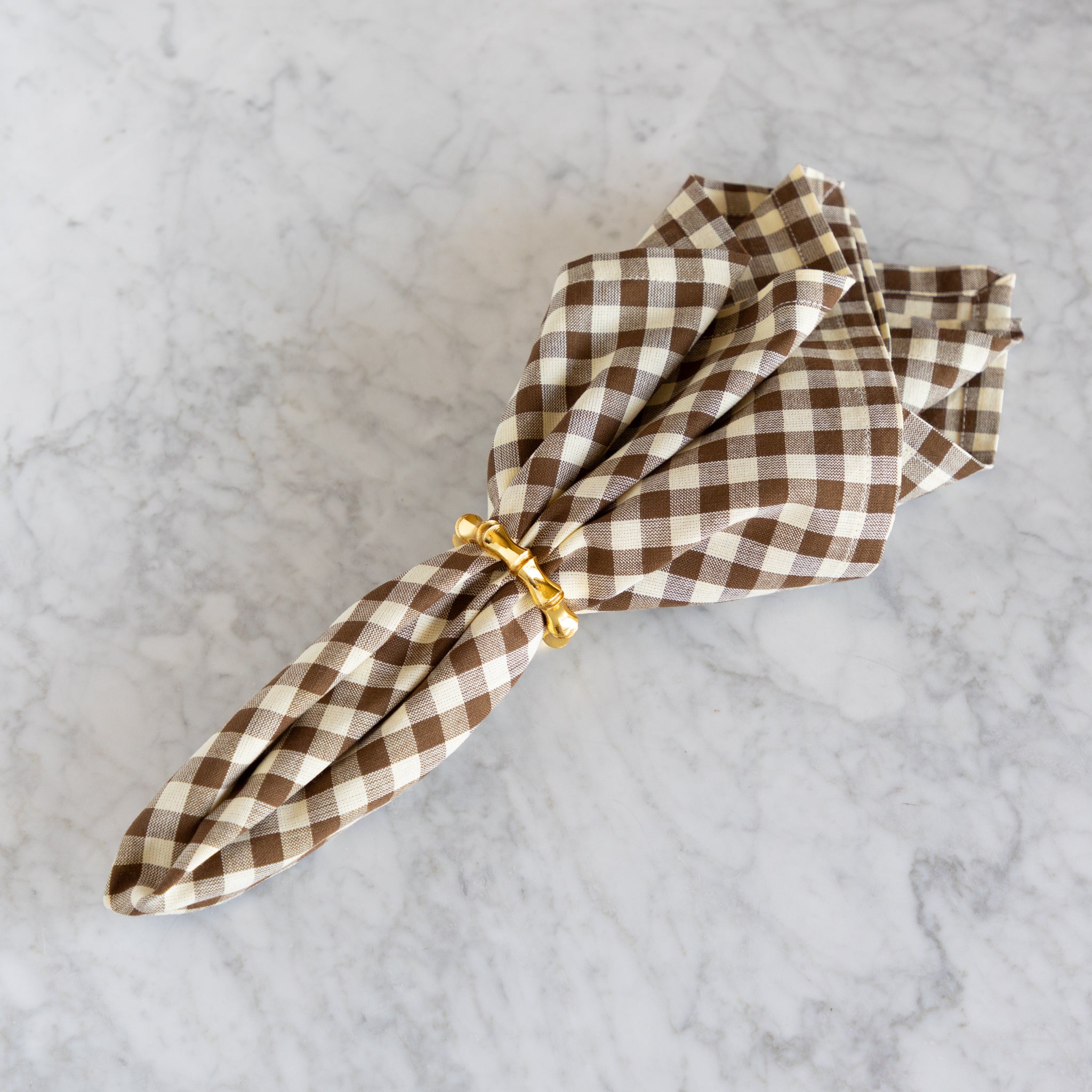Folded brown and white checkered napkin with a gold ring on a marble surface.