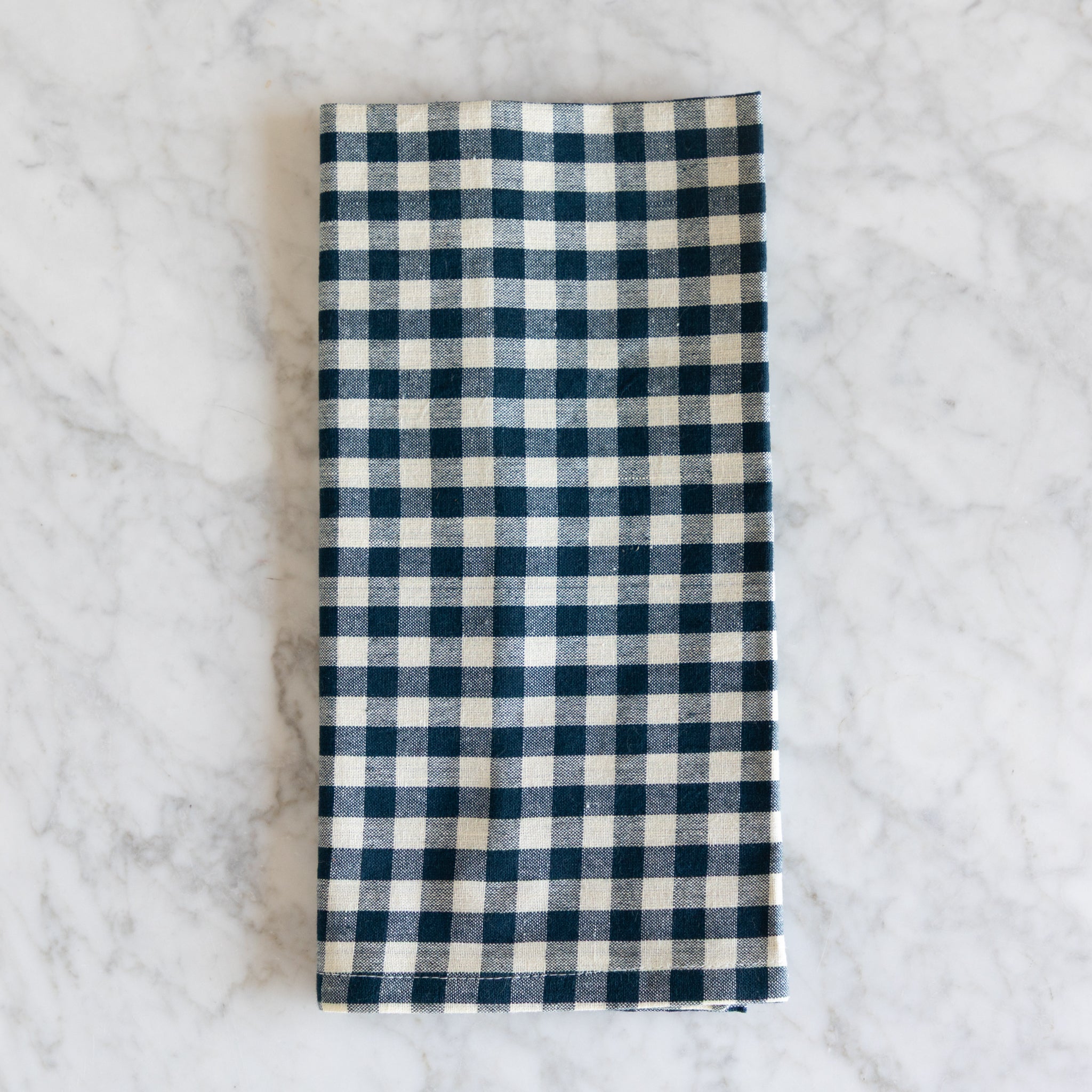 Folded blue and white checkered napkin on a marble surface.