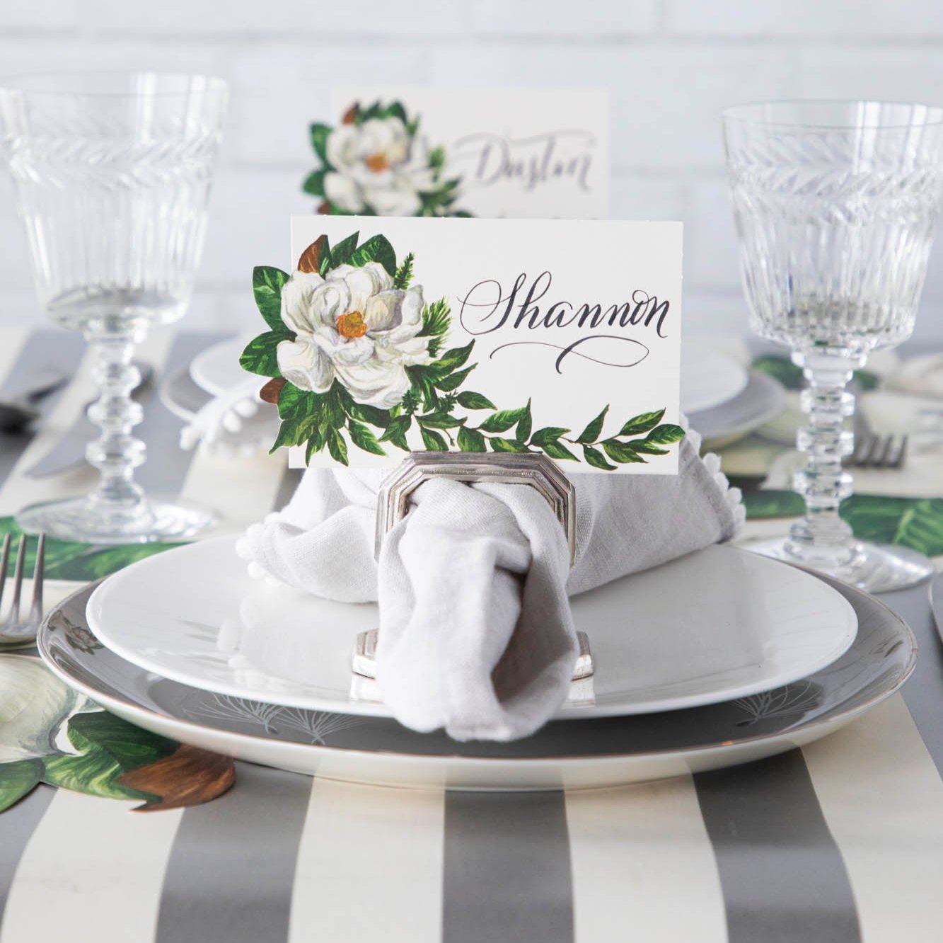 An elegant table setting with the Magnolia Place Card with "Shannon" written on it, inside of a silver napkin ring place card holder.